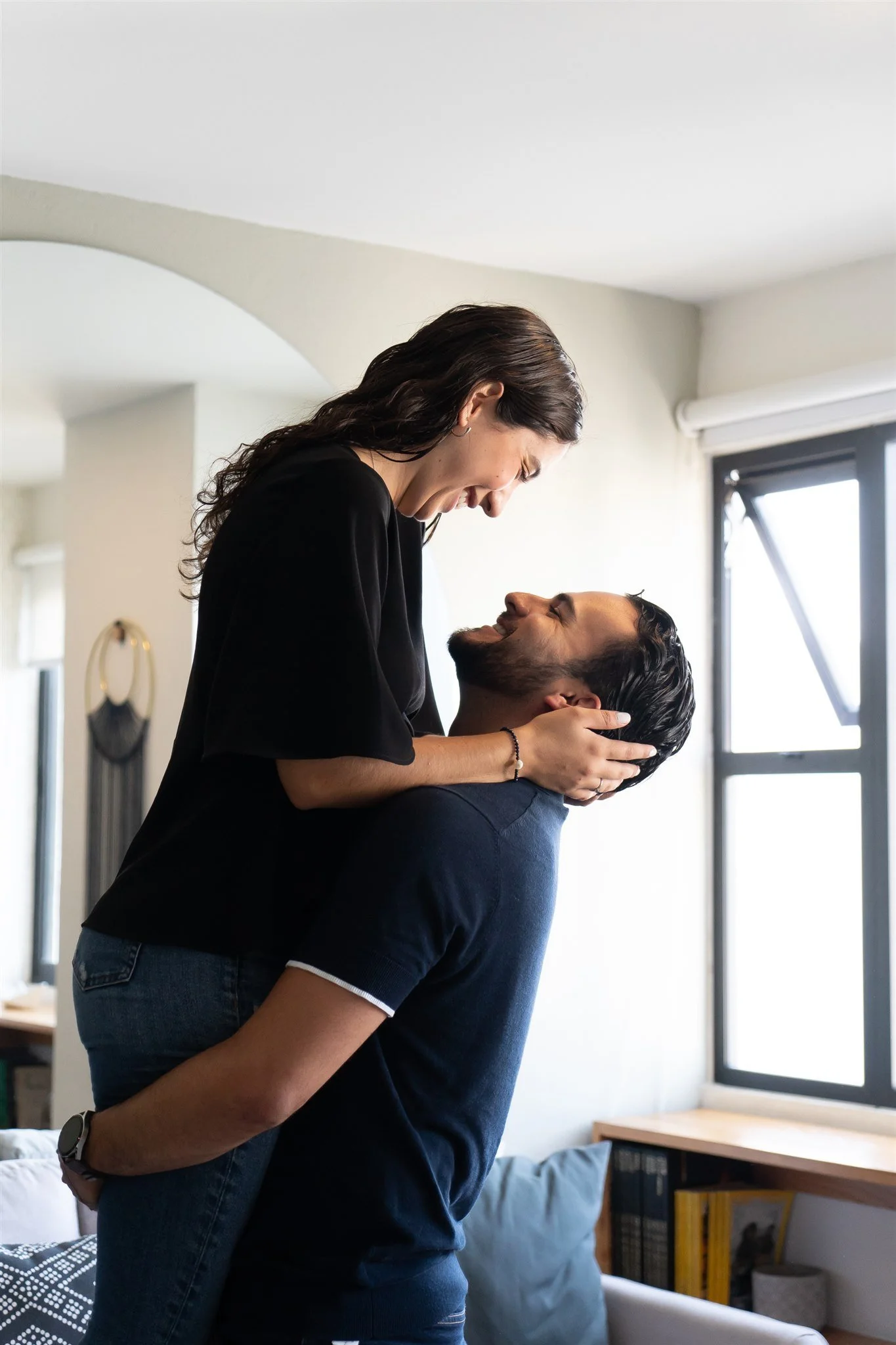 Una pareja feliz en un abrazo en una sala con luz natural y ventanas grandes.