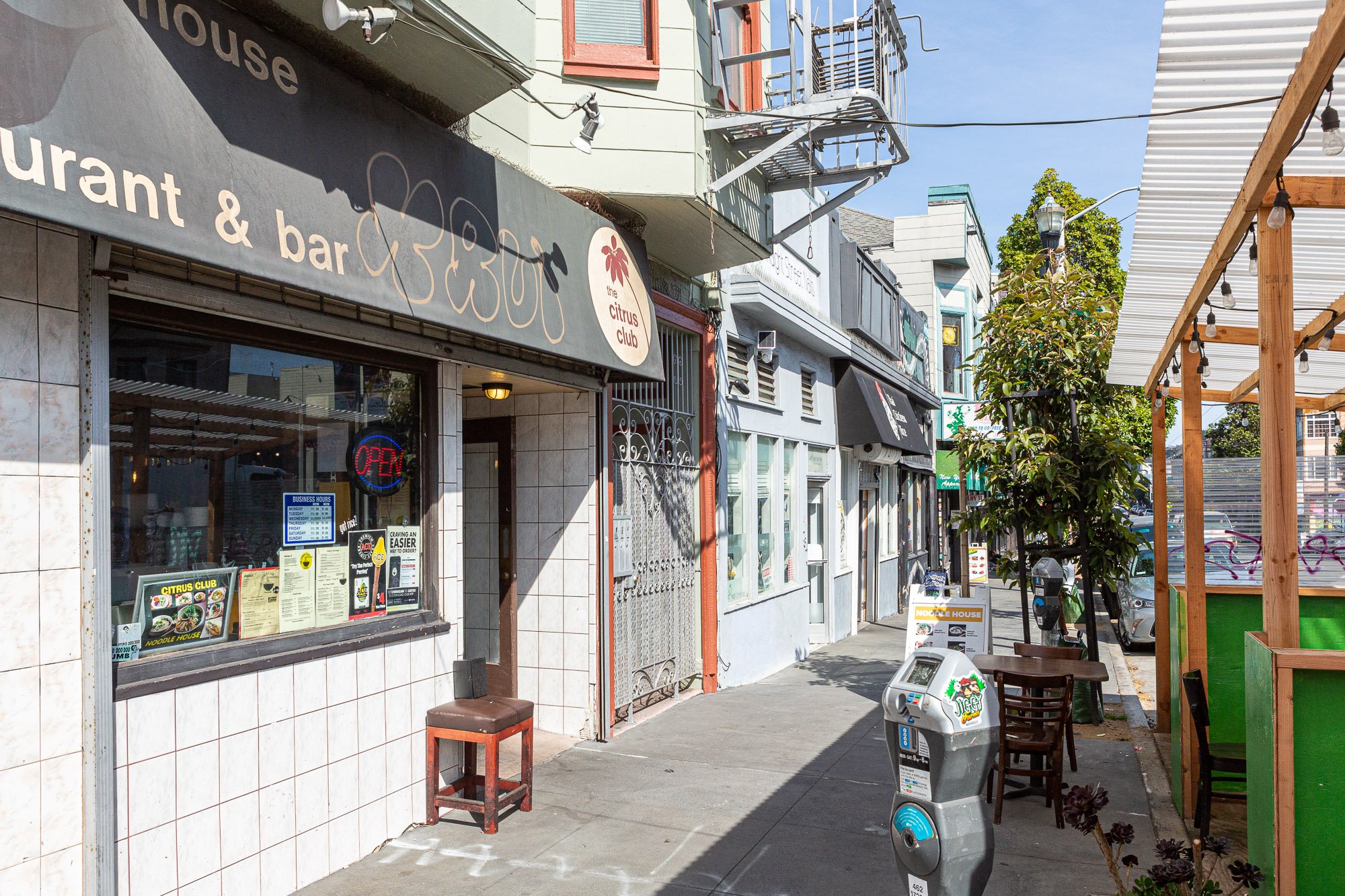 A street view of the Citrus Club restaurant with an open sign, outdoor seating, and nearby buildings in a busy urban area.