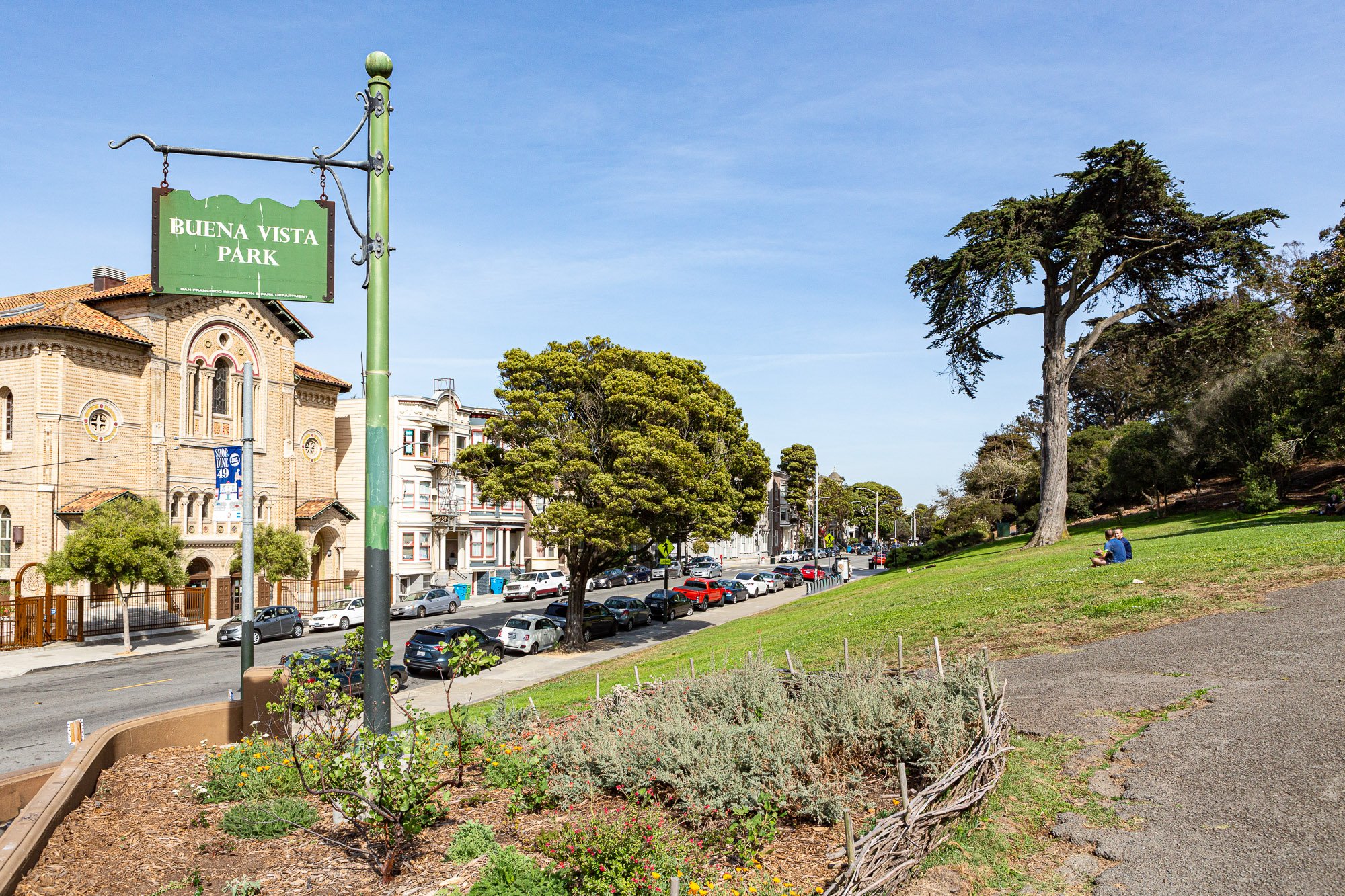 Buena Vista Park sign in a green space with buildings and cars in the background, under a clear blue sky.