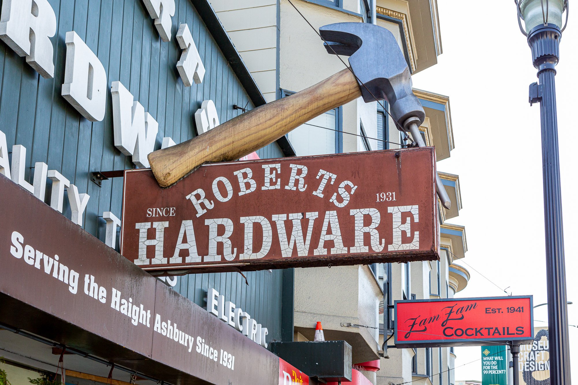 Large hammer-shaped sign for Roberts Hardware, established in 1931, displayed on a building with neighboring signs for Zam Zam Cocktails and other businesses.