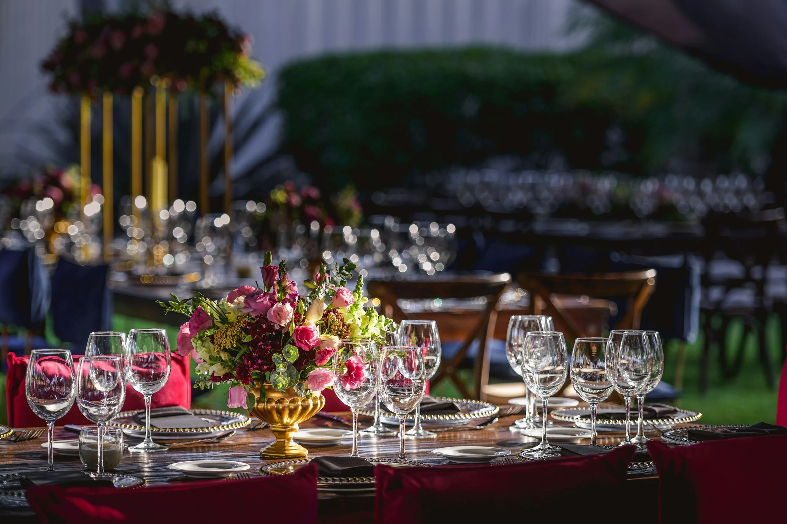 Elegant outdoor dinner table with a floral centerpiece, glassware, and decorated with gold accents at sunset or evening.