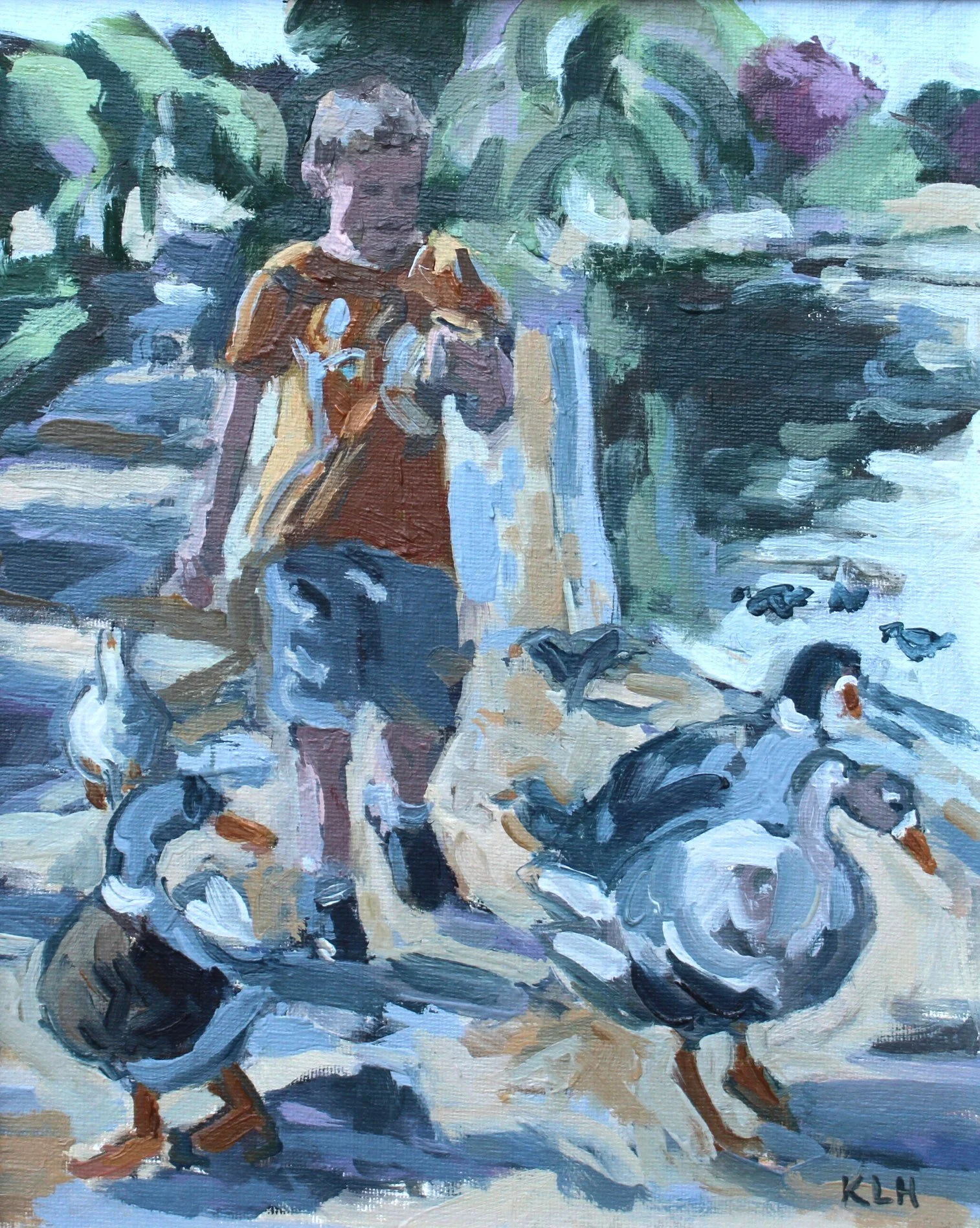 A young boy in a yellow T-shirt and shorts standing outdoors surrounded by ducks, with lush greenery in the background.