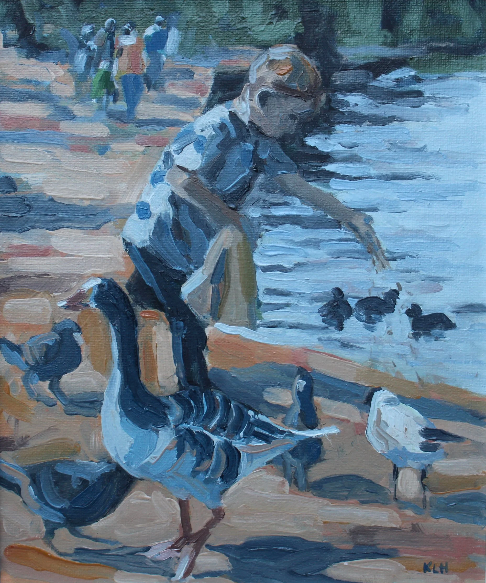 A young boy in glasses, wearing a striped polo shirt, is crouching near the water at the beach with ducks. In the background, a group of people is walking along the shoreline.