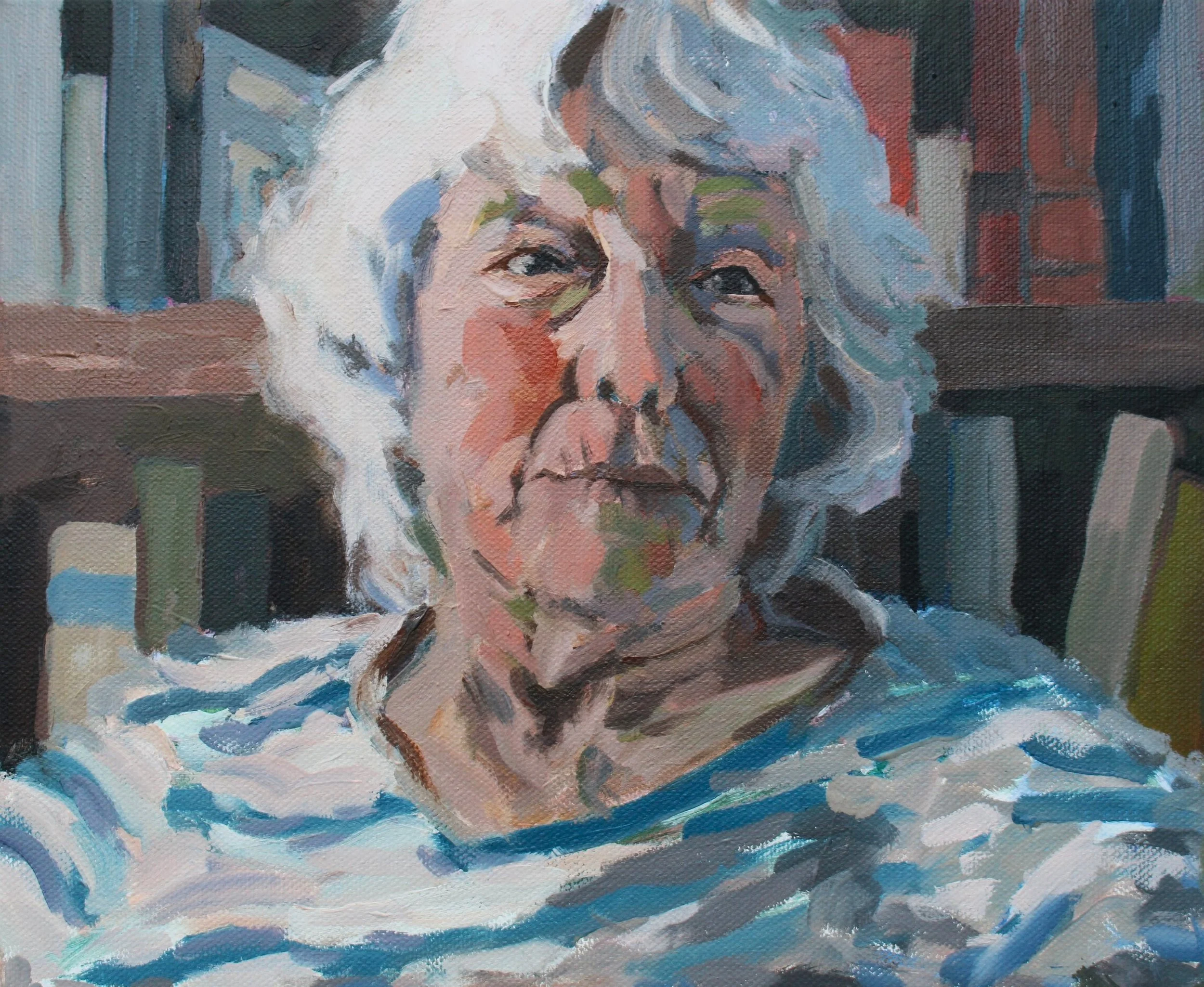 A portrait of an elderly woman with white hair, wearing a striped shirt, sitting in front of a bookshelf.