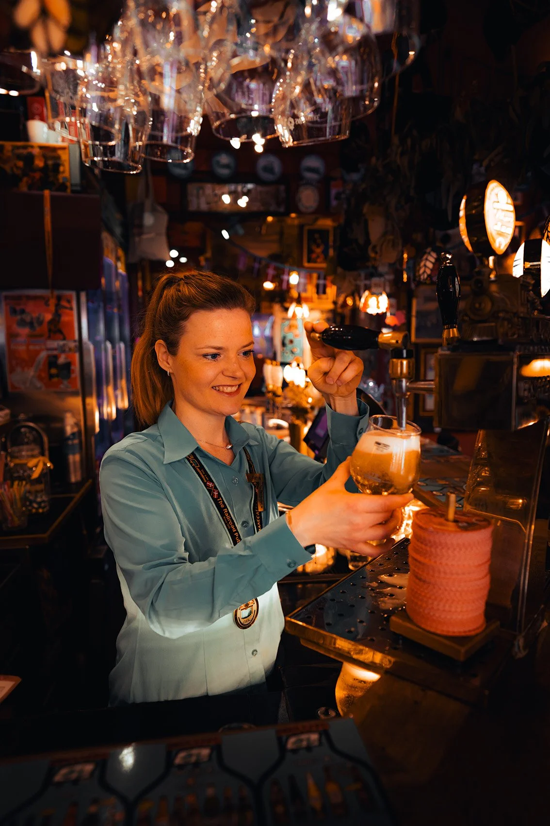 En kvinde, der serverer en øl på en bar fyldt med lys og dekorationer.