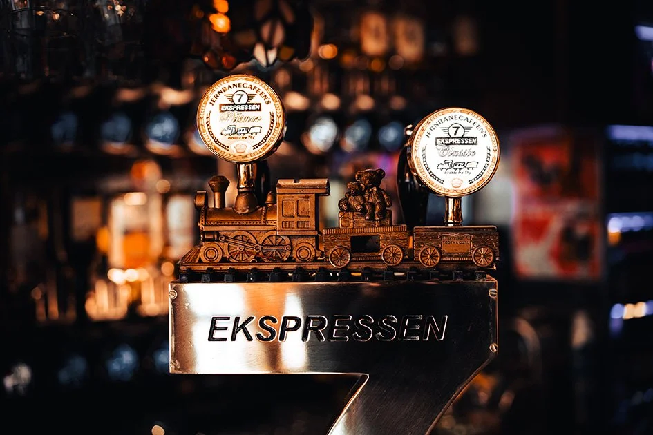 En bar med et klart ankersymbol med teksten "EKSPRESSEN" under. Der er en juleagtig togfigur på toppen af ankersymbolet.