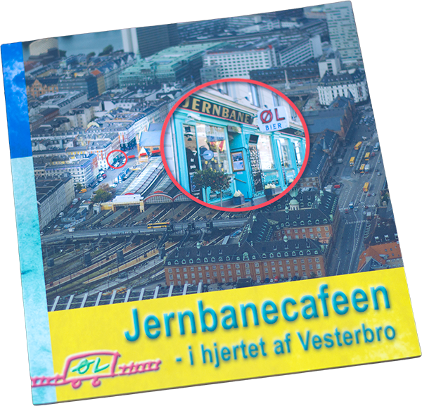 Flyvefoto af en by med et forstørret billede af en café, Jernbanecafeen, i centrum, beliggende ved Vesterbro med togbaner i nærheden.