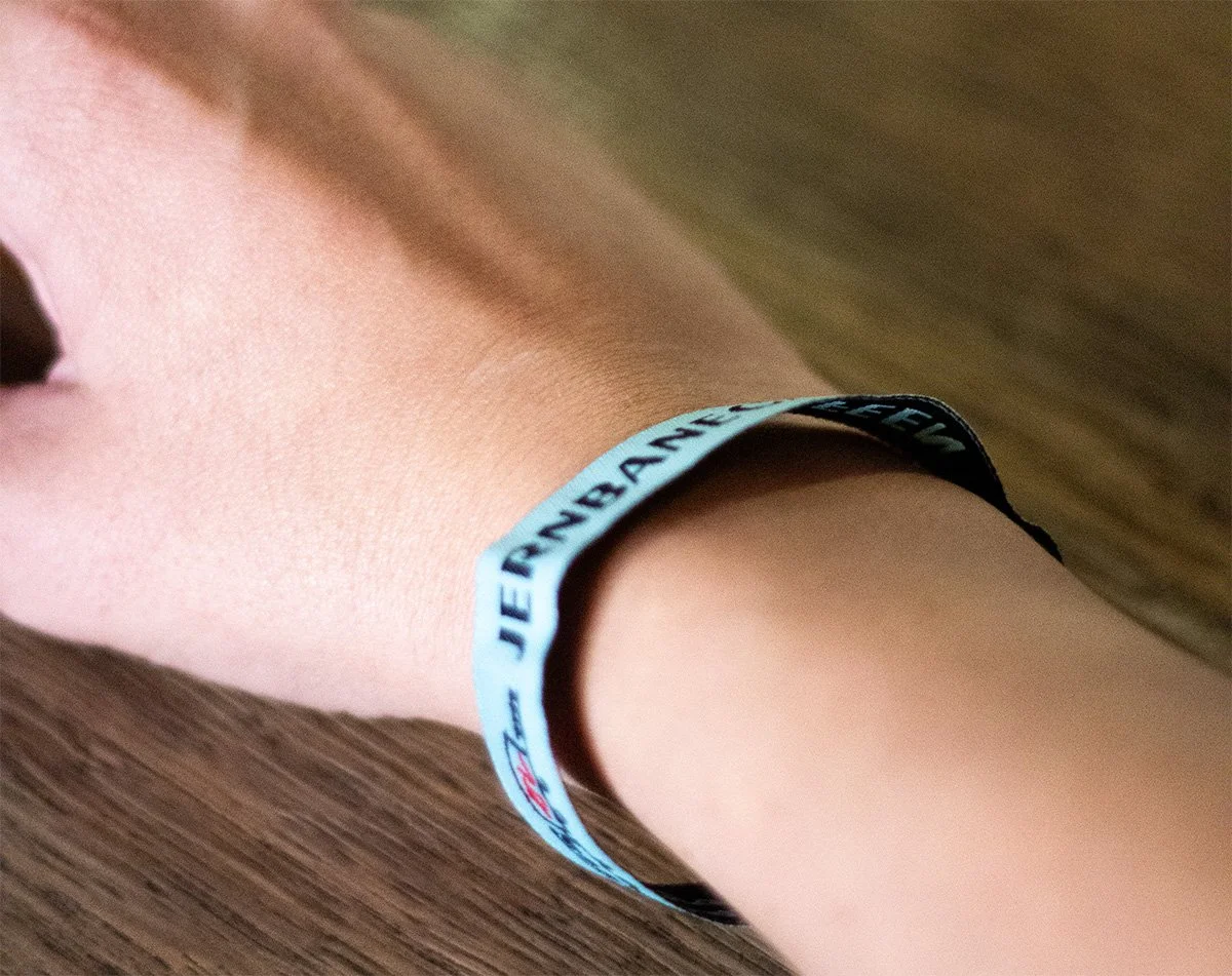 Nærbillede af en persons arm med en lys blå armbånd, der har tekst på, på en træbord.
