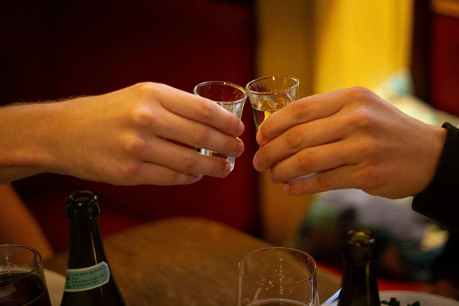 To personer skåler med små glas alkoholholdige drikkevarer på en bar.