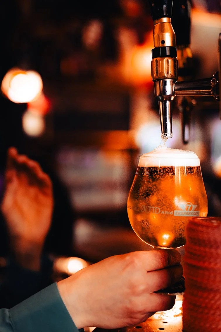 Et glas øl under en ølhaner i en bartender eller barpersons hånd, med skum på toppen og boblende i glasset.