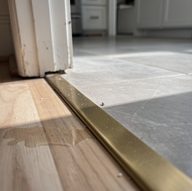 A metal threshold separates wooden flooring from tile flooring at a doorway with white door frame.