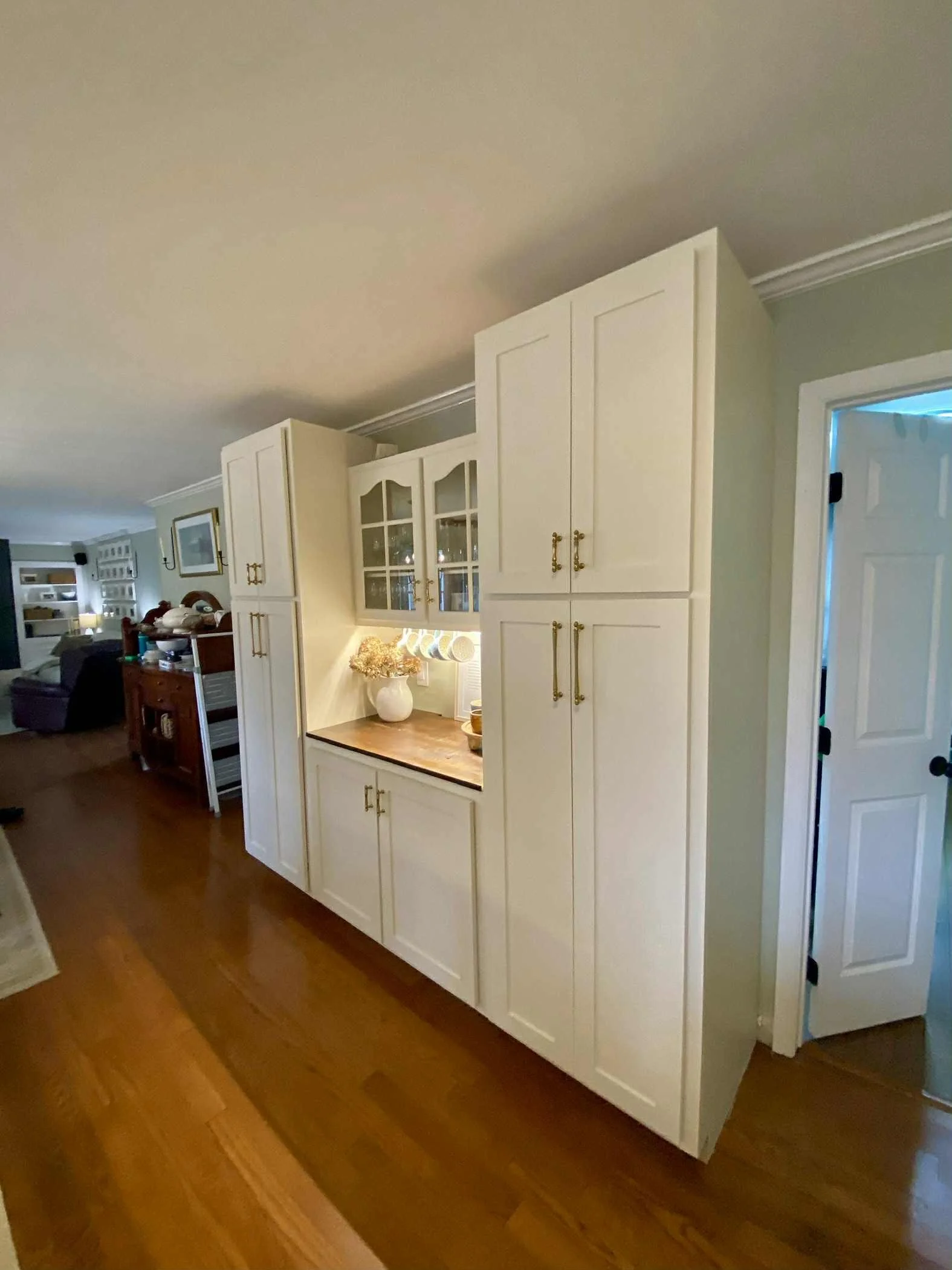 White kitchen cabinet with gold handles next to a doorway in a living room with wooden flooring.