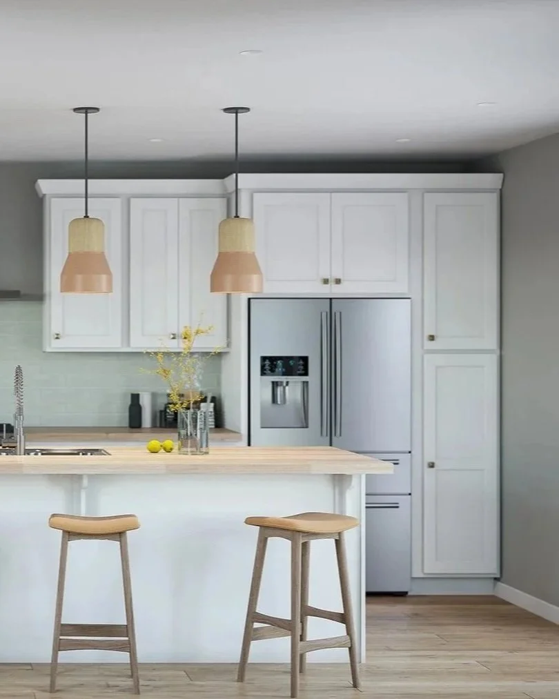 Modern kitchen with white cabinets, stainless steel refrigerator, wooden island with two bar stools, two pendant lights, light wood flooring, and minimalist decor.