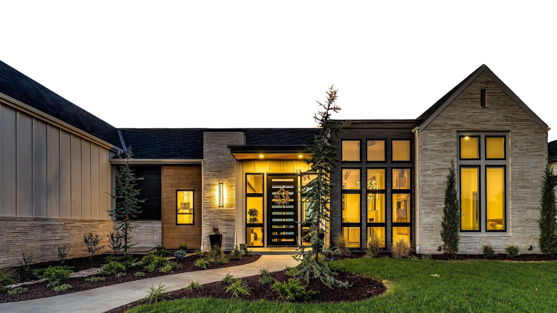 Modern house exterior at night with illuminated interior, landscaped front yard, pathway, and trees.