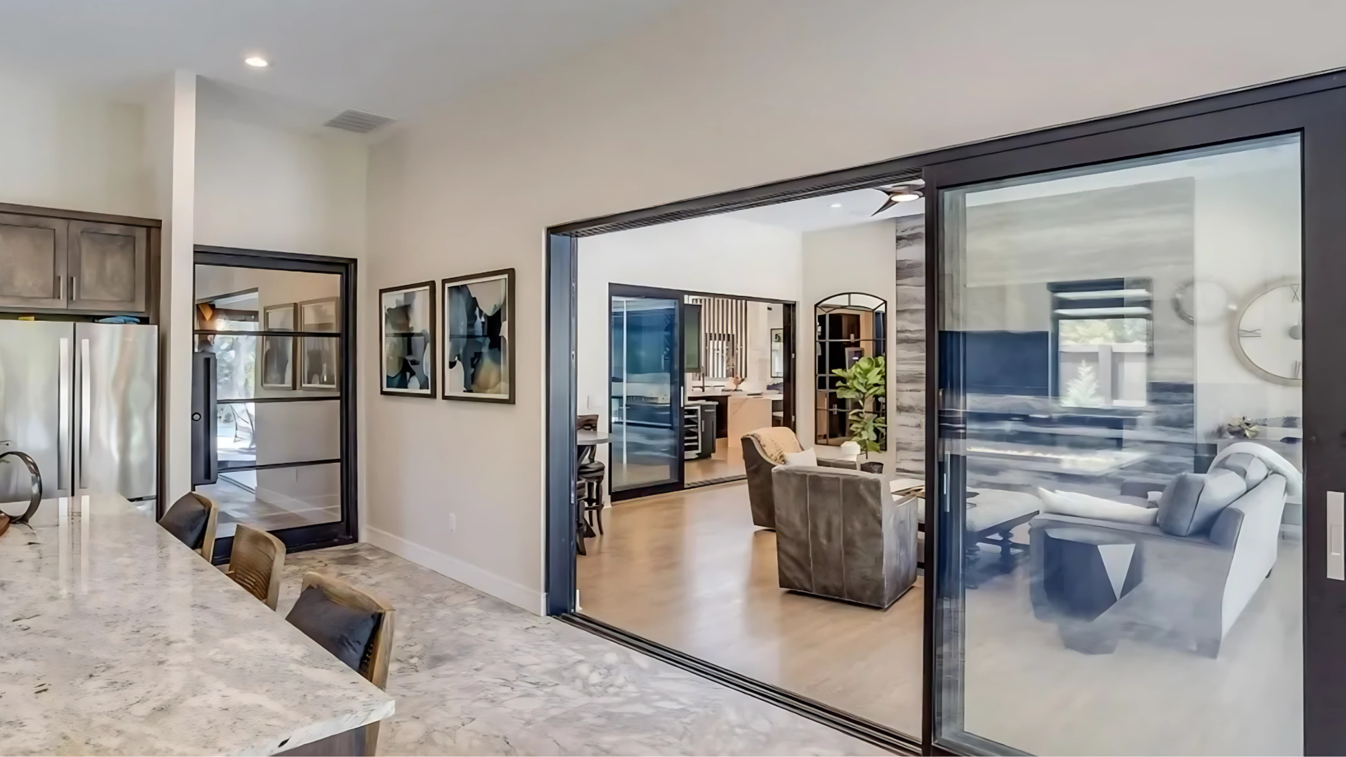 Modern open-concept kitchen and living room with sliding glass doors, wooden flooring, framed artwork, kitchen island, and comfortable seating areas.