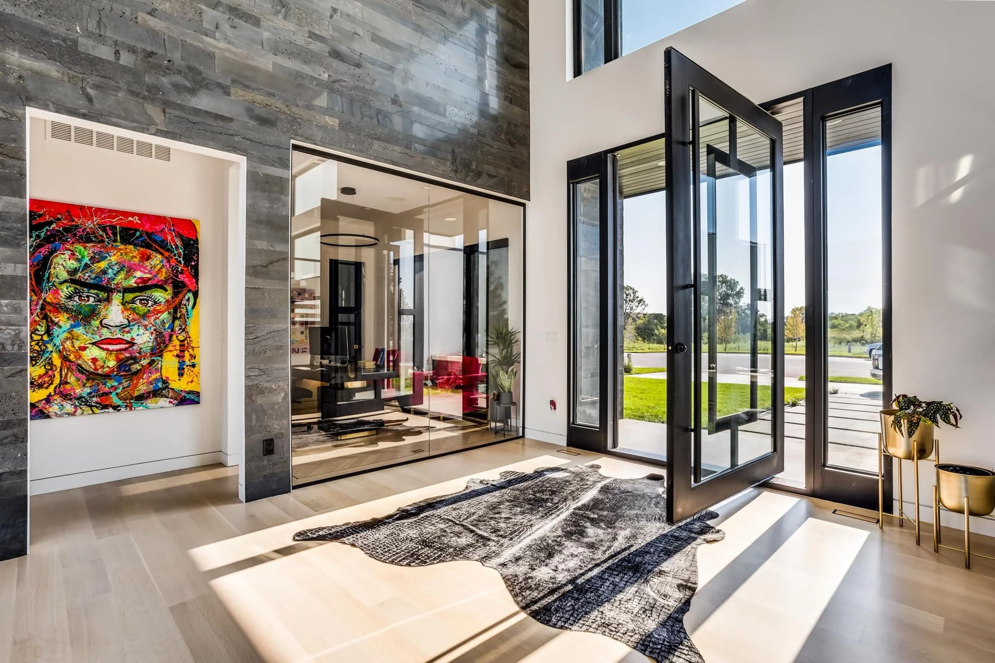 Modern interior living space with large glass doors, artistic colorful portrait on wall, and a cowhide rug on light wood floor.