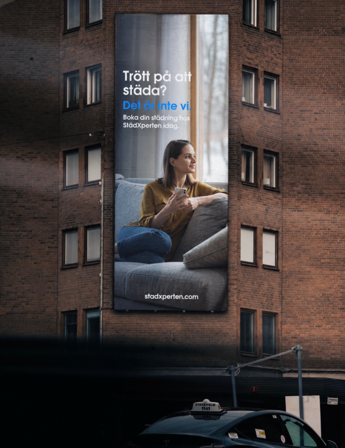 En reklamannons på en byggnad för städningstjänster, med en bild av en kvinna som sitter på en soffa och använder sin mobil.