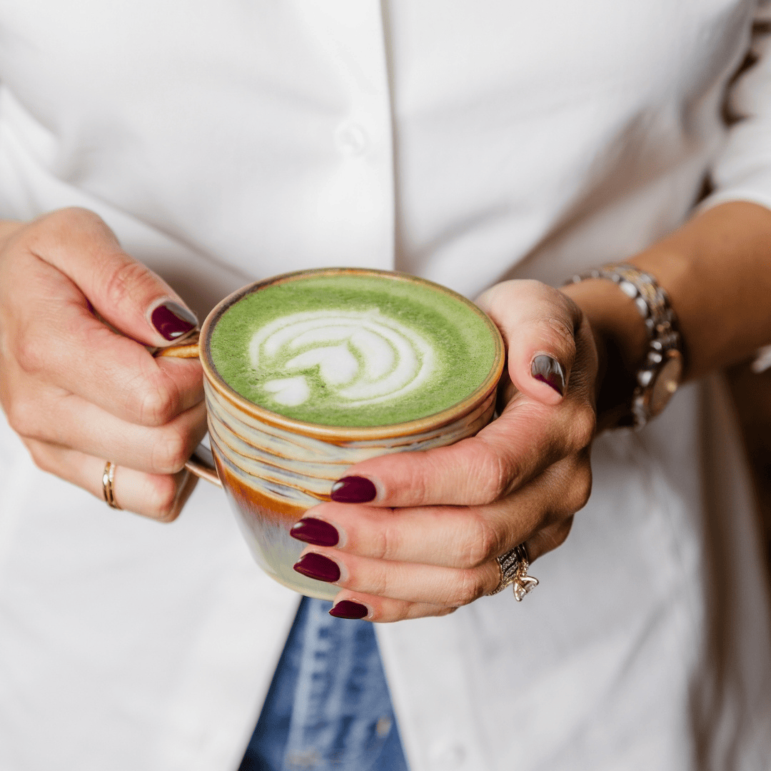 Person holding a green matcha latte with latte art in a ceramic cup.