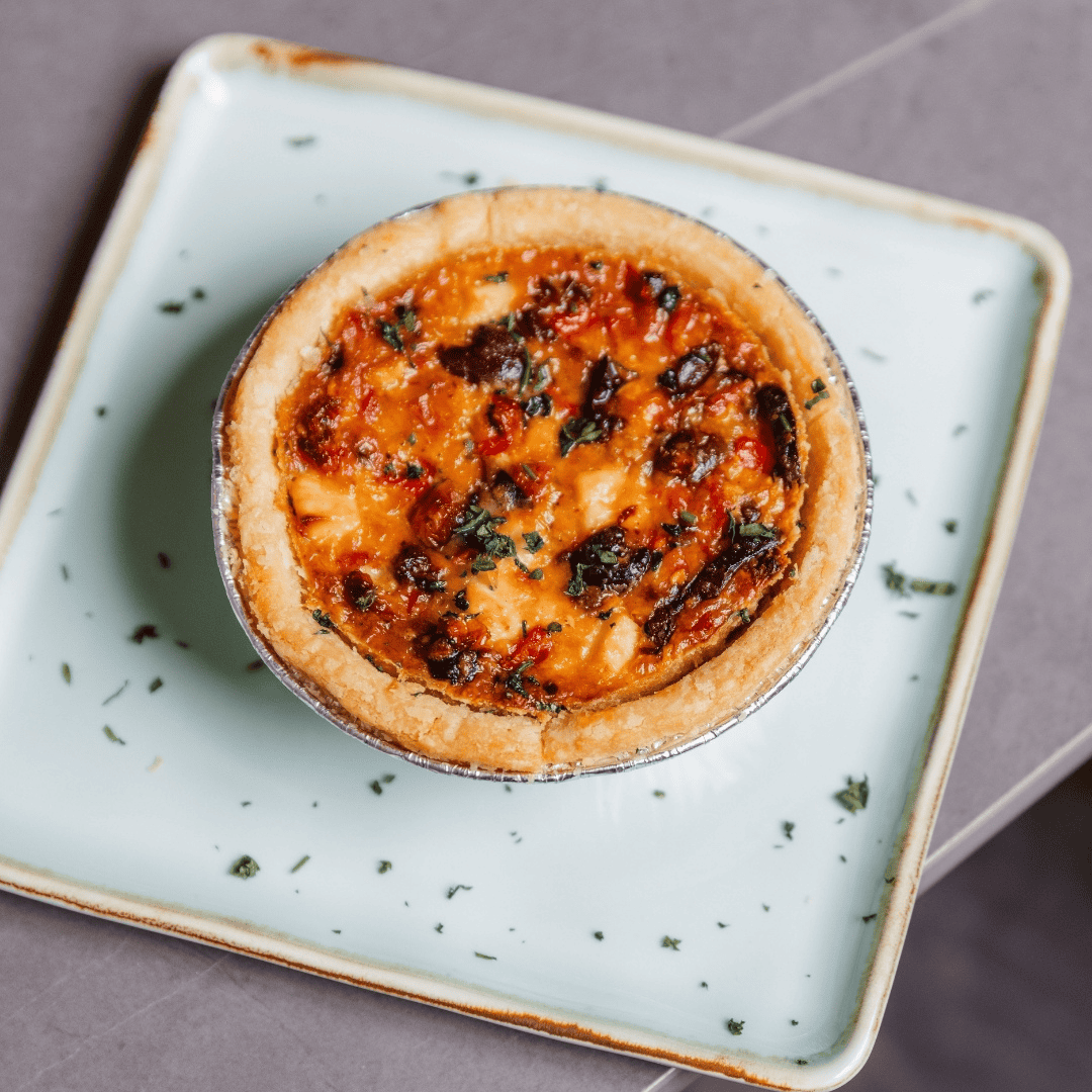 A mini meat pie with a golden crust and a vegetable and meat filling on a square, pale green plate with herbs.