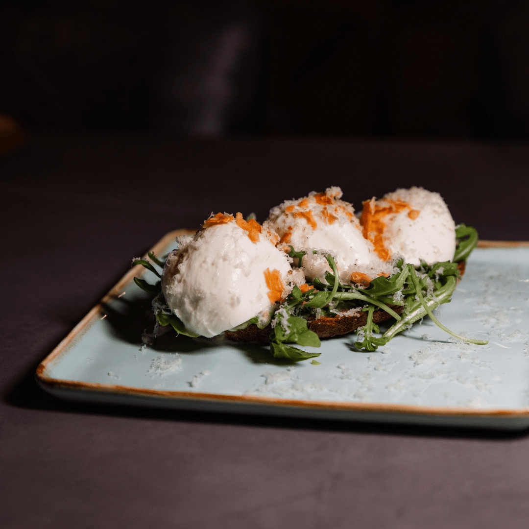 Three poached eggs topped with orange seasoning on a bed of greens, served on a ceramic plate.