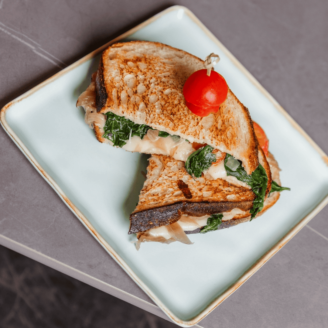 Grilled sandwich with spinach and melted cheese, topped with a cherry tomato on a light green plate.