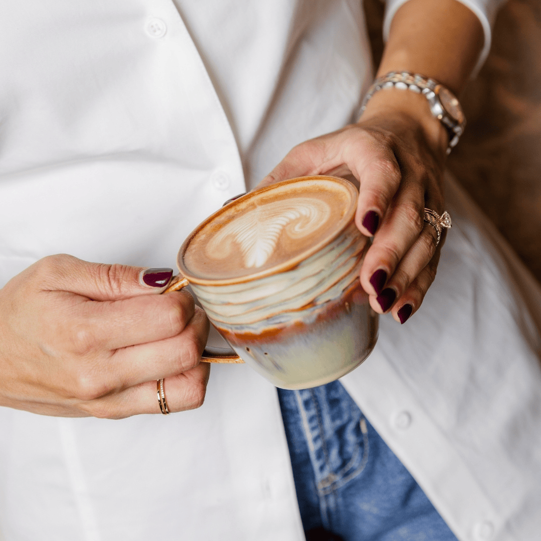 Person holding a ceramic coffee mug with latte art.