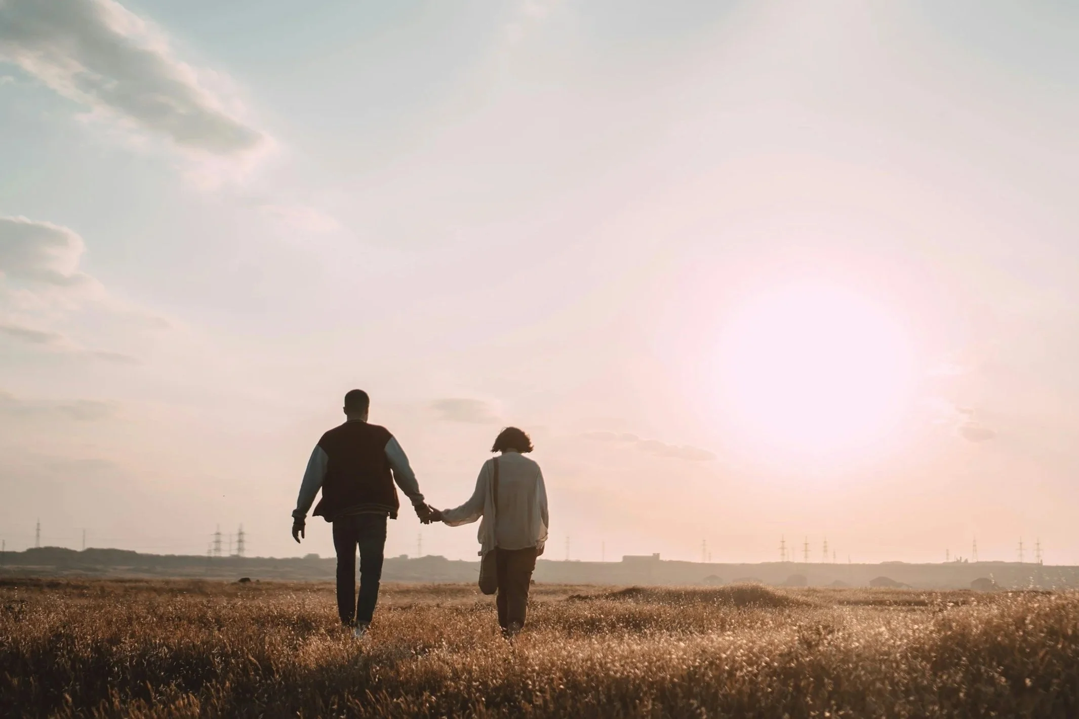 a couple walk in a field towards the sun