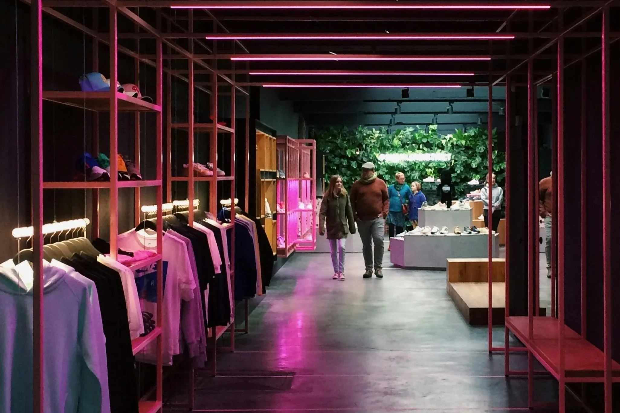 Modern retail space with pink lighting, showcasing clothing on racks, and a vibrant green wall in the background.