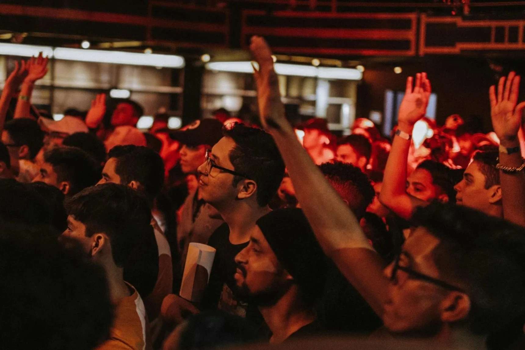 A lively crowd at a concert with hands raised, vibrant lights, and a festive atmosphere, creating an energetic vibe.