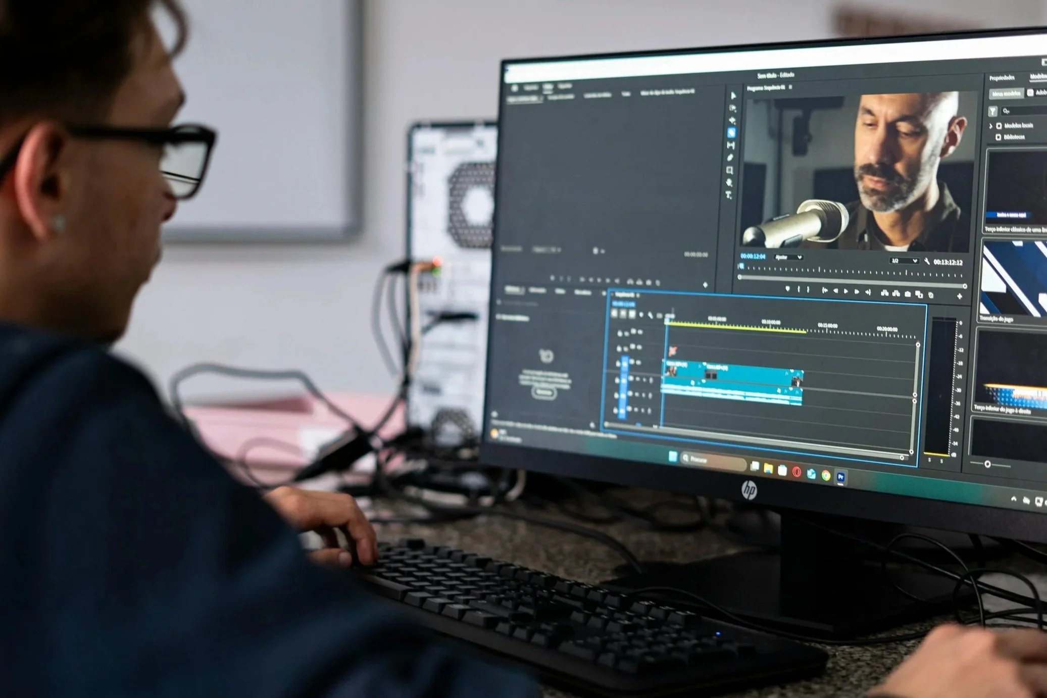 A person is editing video footage on a computer, with audio equipment visible on the screen in a modern workspace.