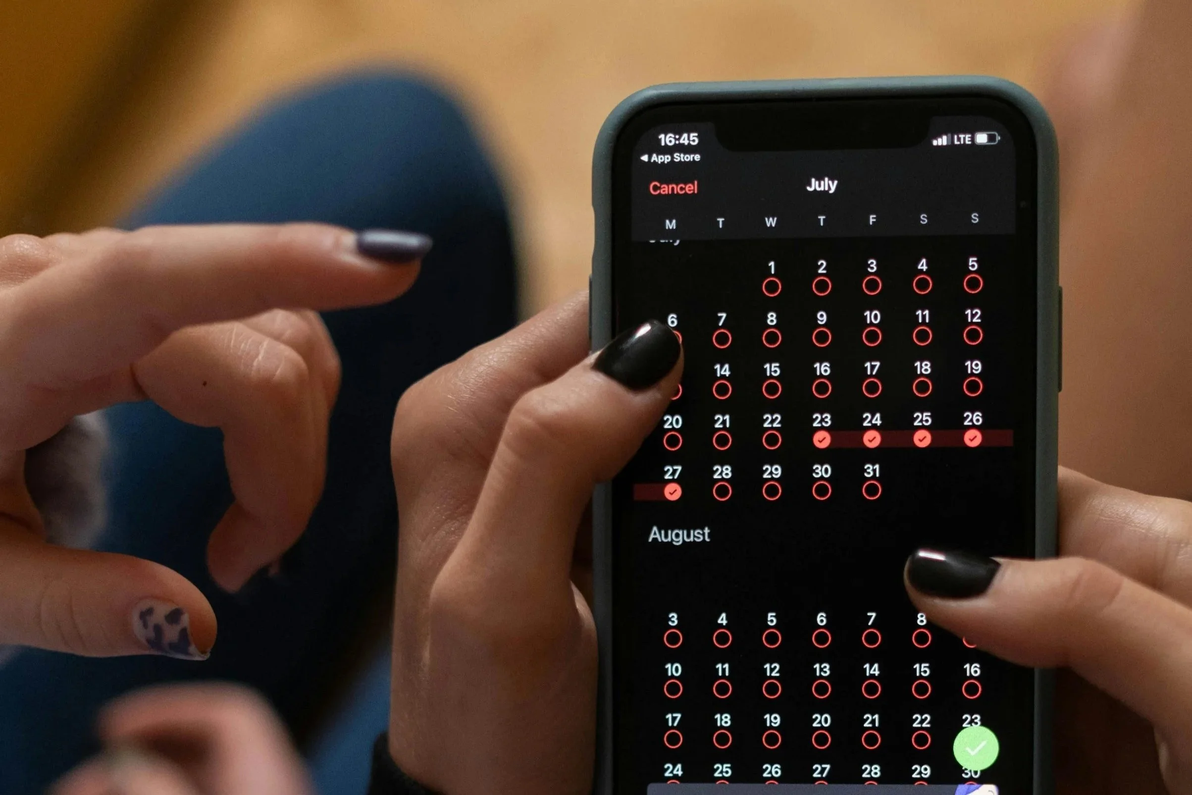 A close-up of two hands interacting with a smartphone displaying a calendar app, focusing on July and August dates.