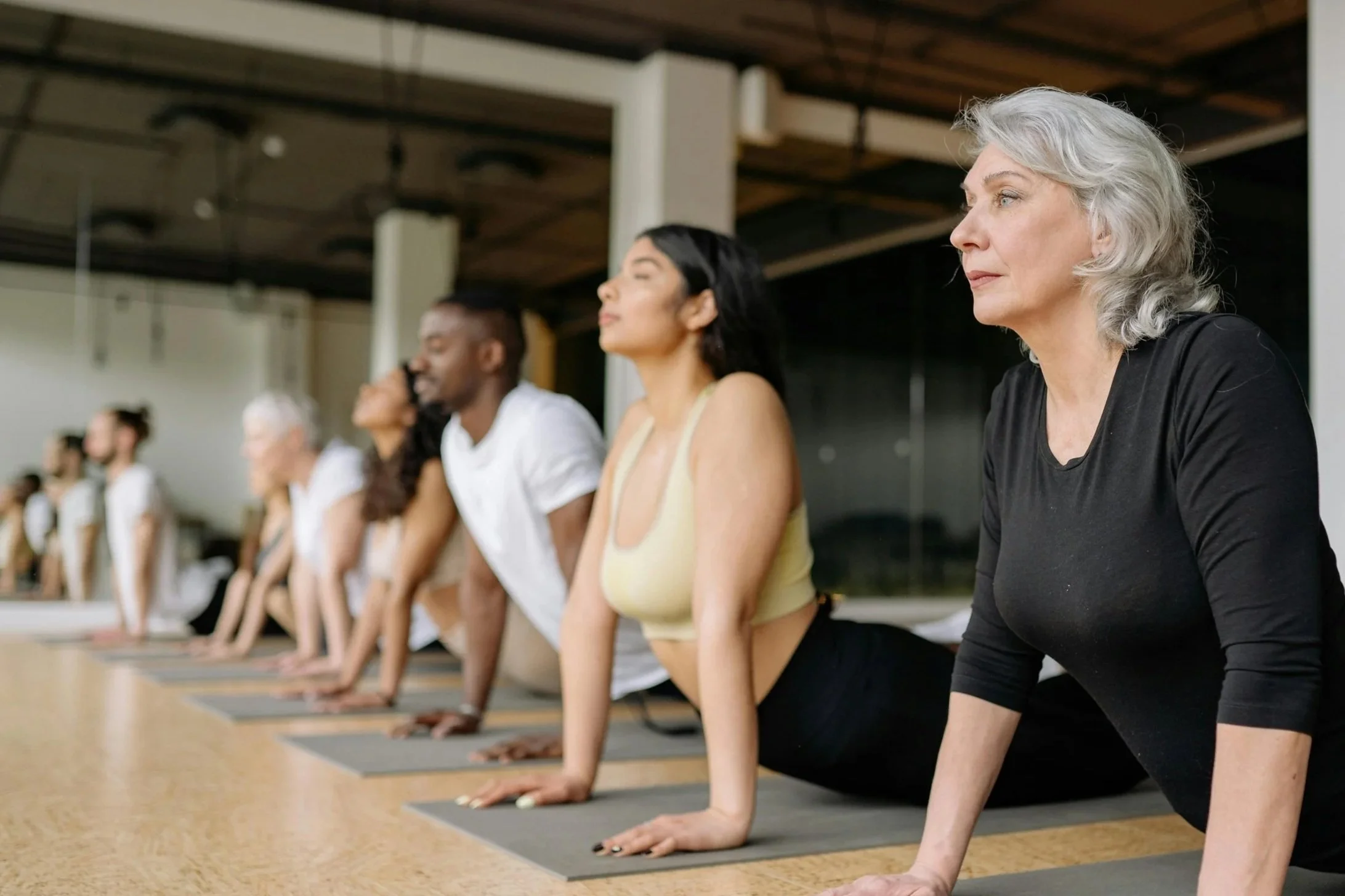 Group of diverse people practicing yoga in upward dog pose on mats in a bright studio.