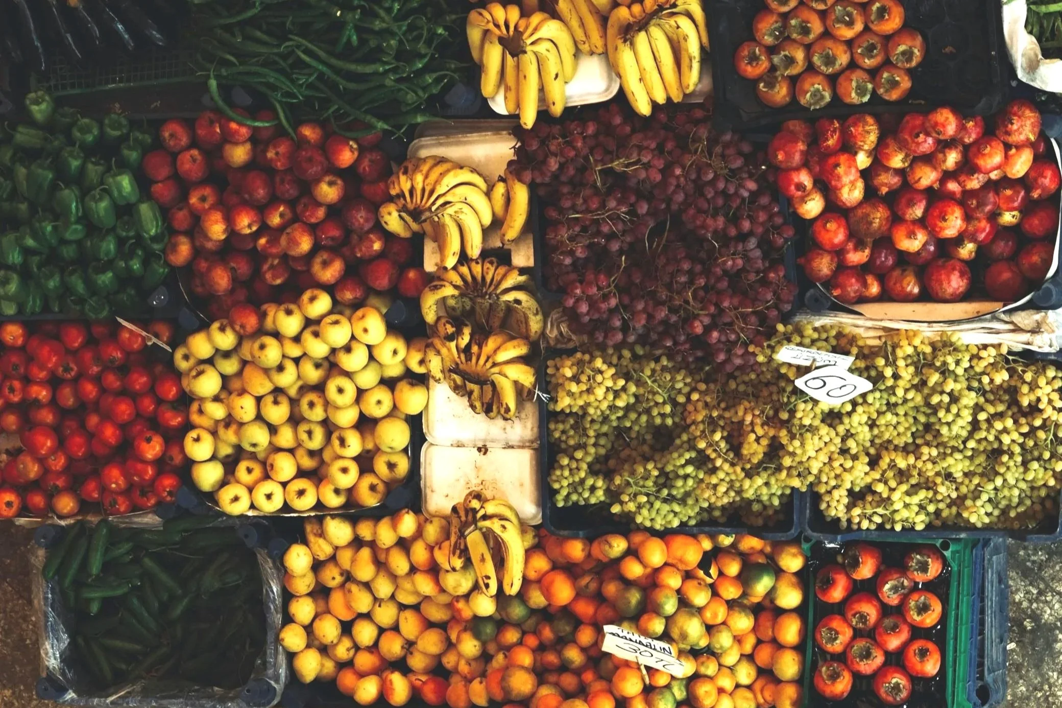 Aerial view of a vibrant market stall filled with diverse fruits including bananas, apples, oranges, and grapes, with a shopper selecting items.