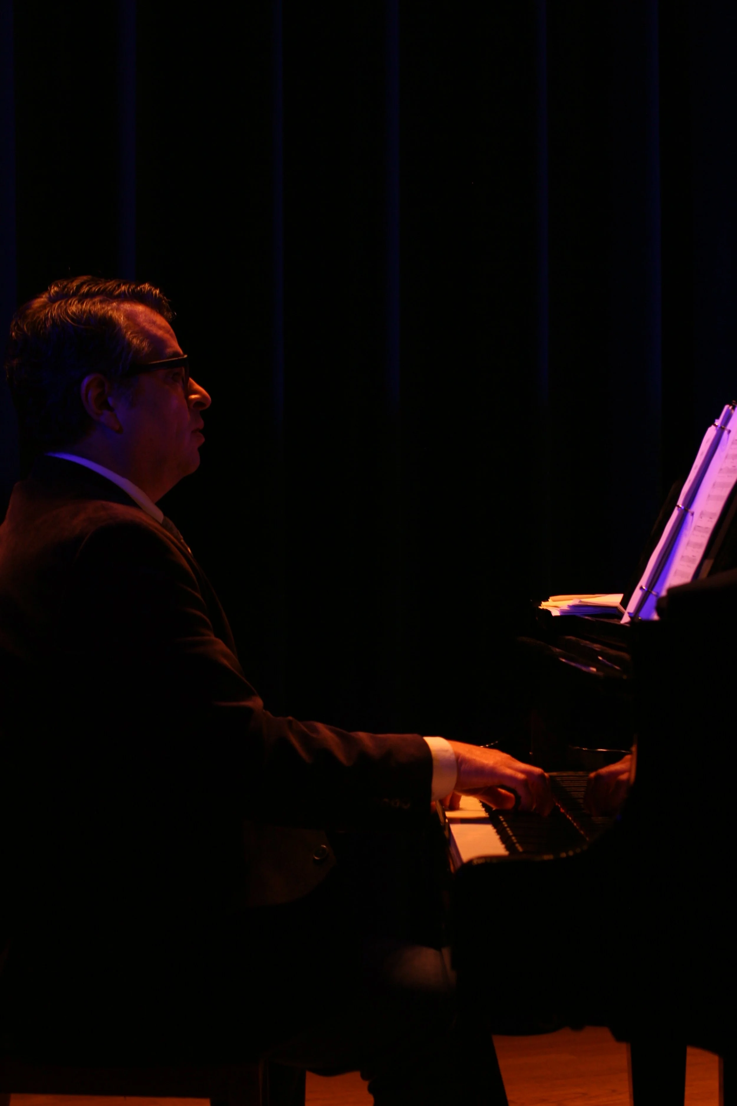 Man playing a grand piano on stage in dim lighting.