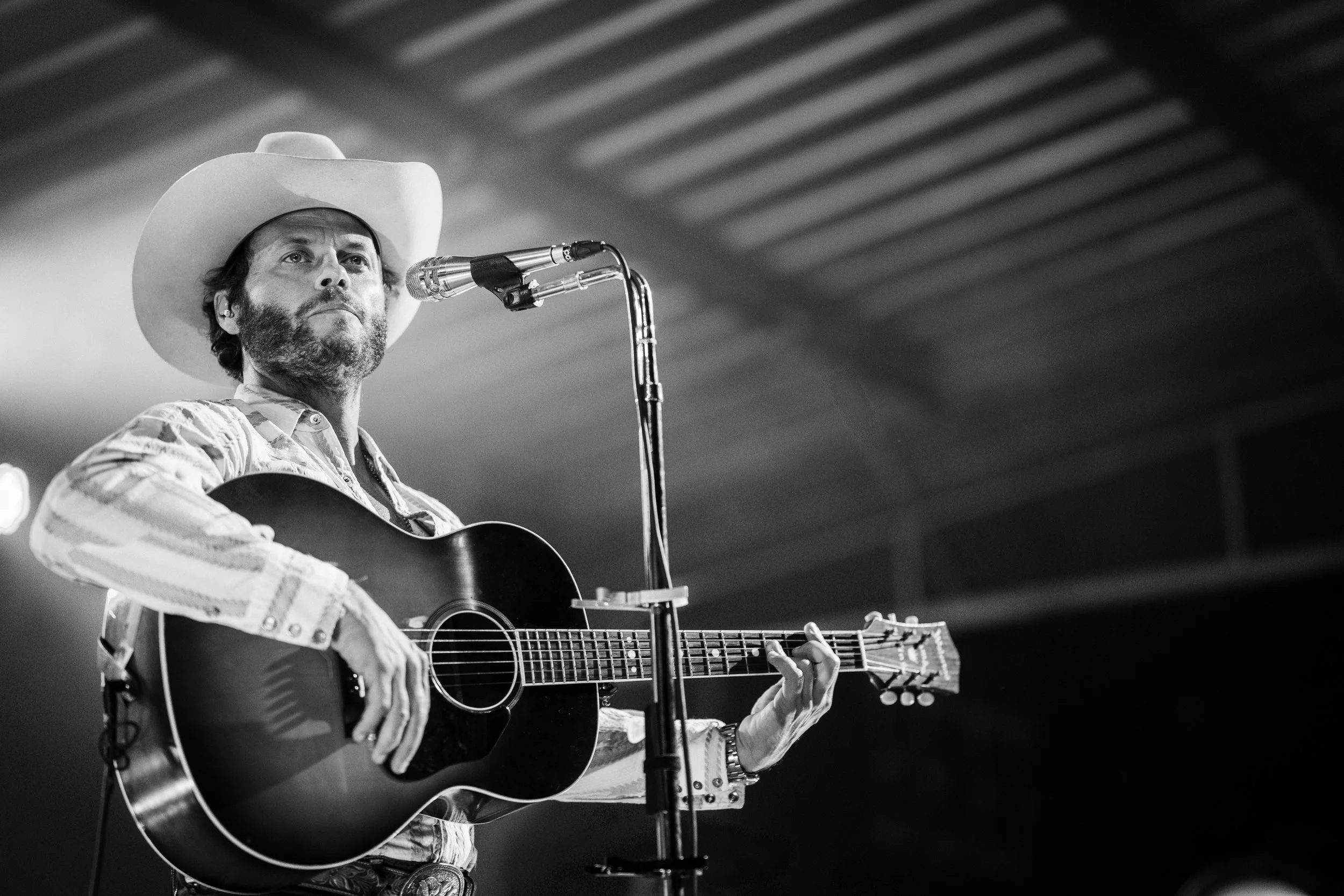 Charley Crockett | A man wearing a cowboy hat playing an acoustic guitar and singing into a microphone.