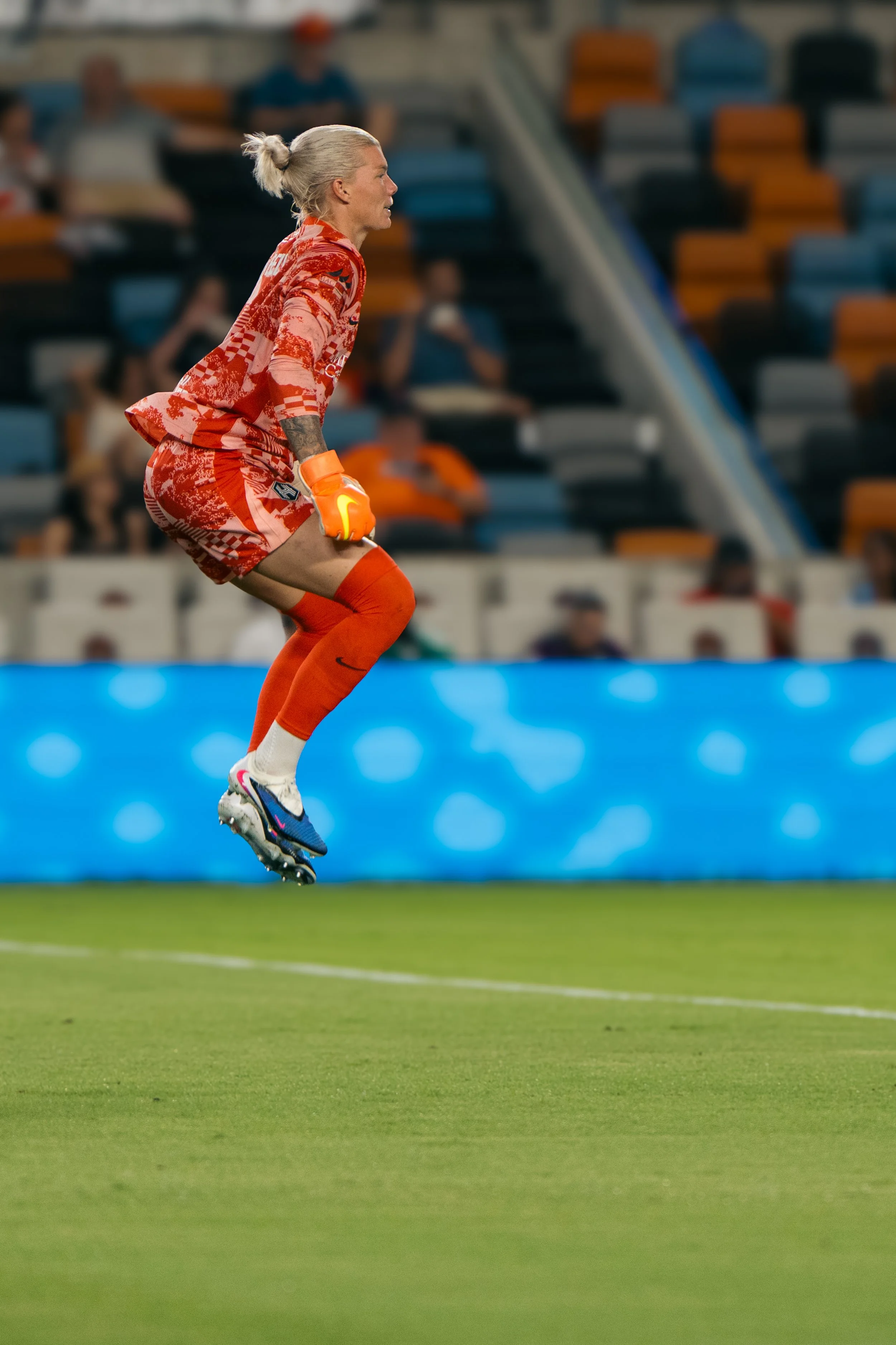 Houston Dash | A female soccer goalkeeper in a red uniform jumping to catch a ball during a game.