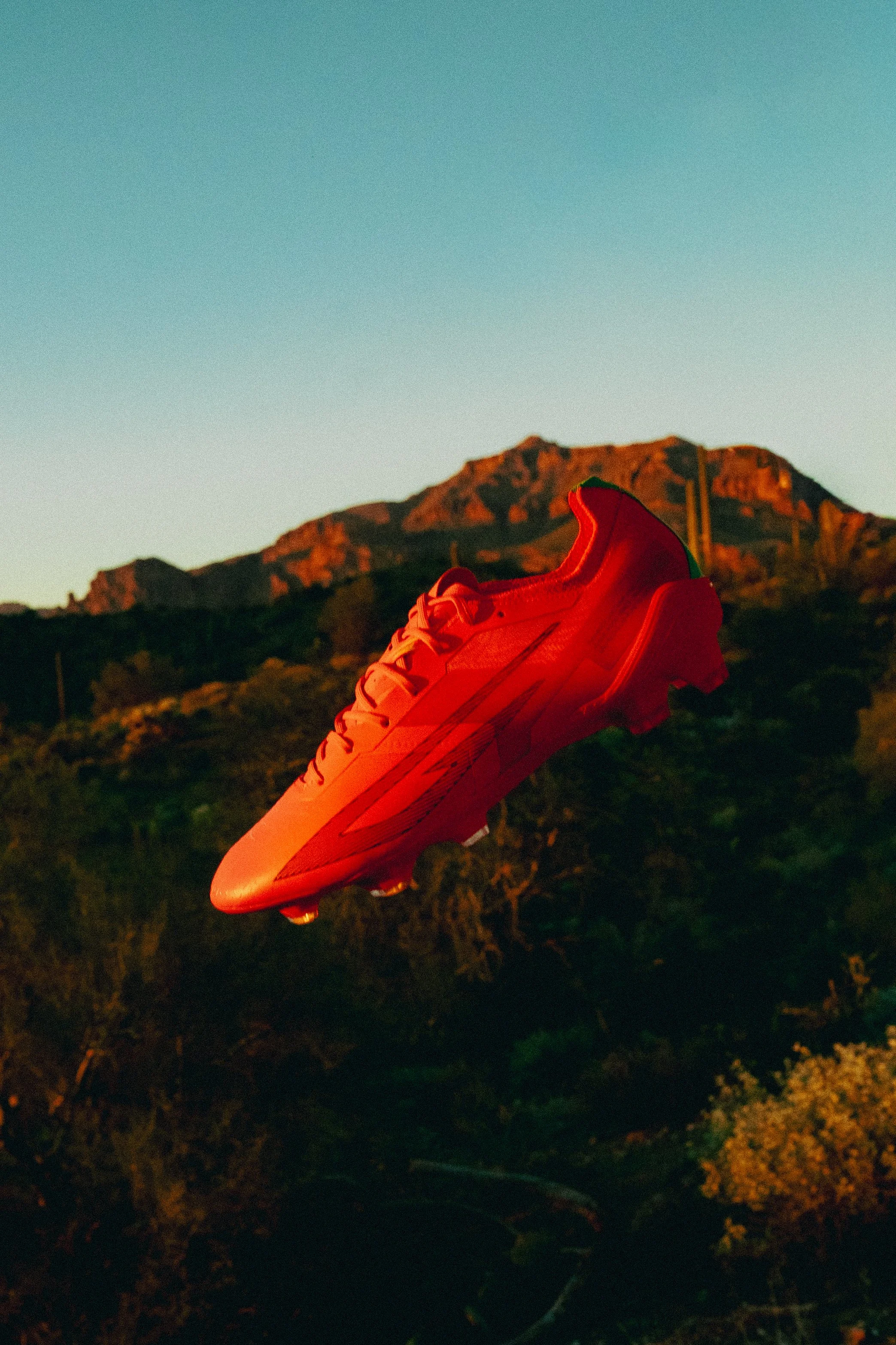 Red soccer cleat shoe floating over a landscape with mountains and sky in the background.