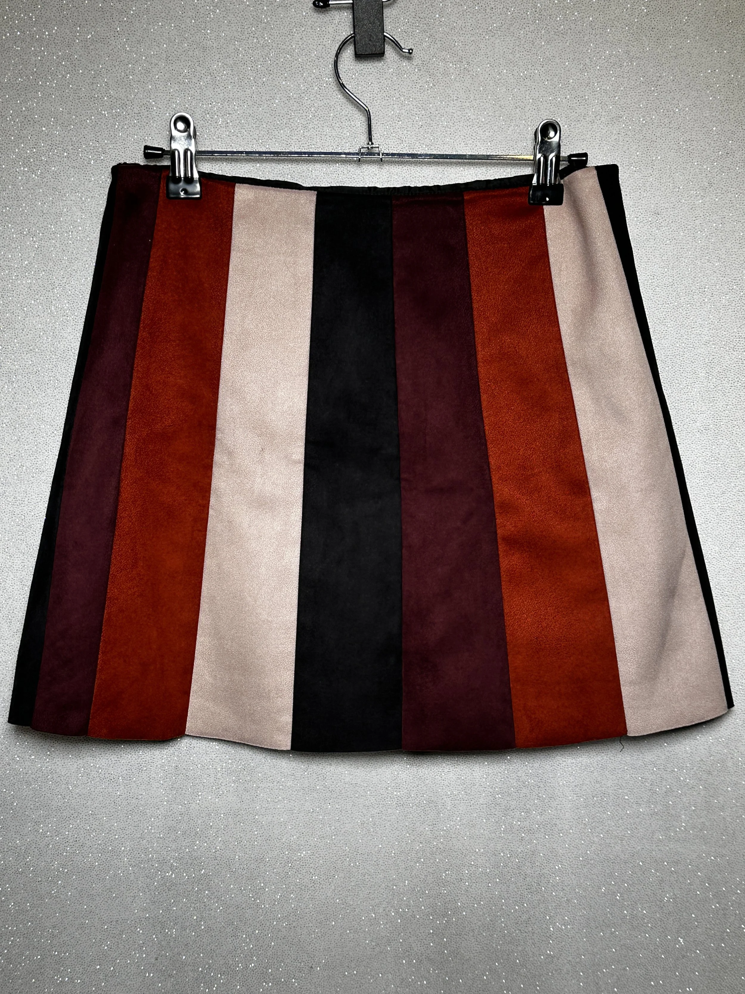 Colorful striped skirt hanging on a wall with a clip.