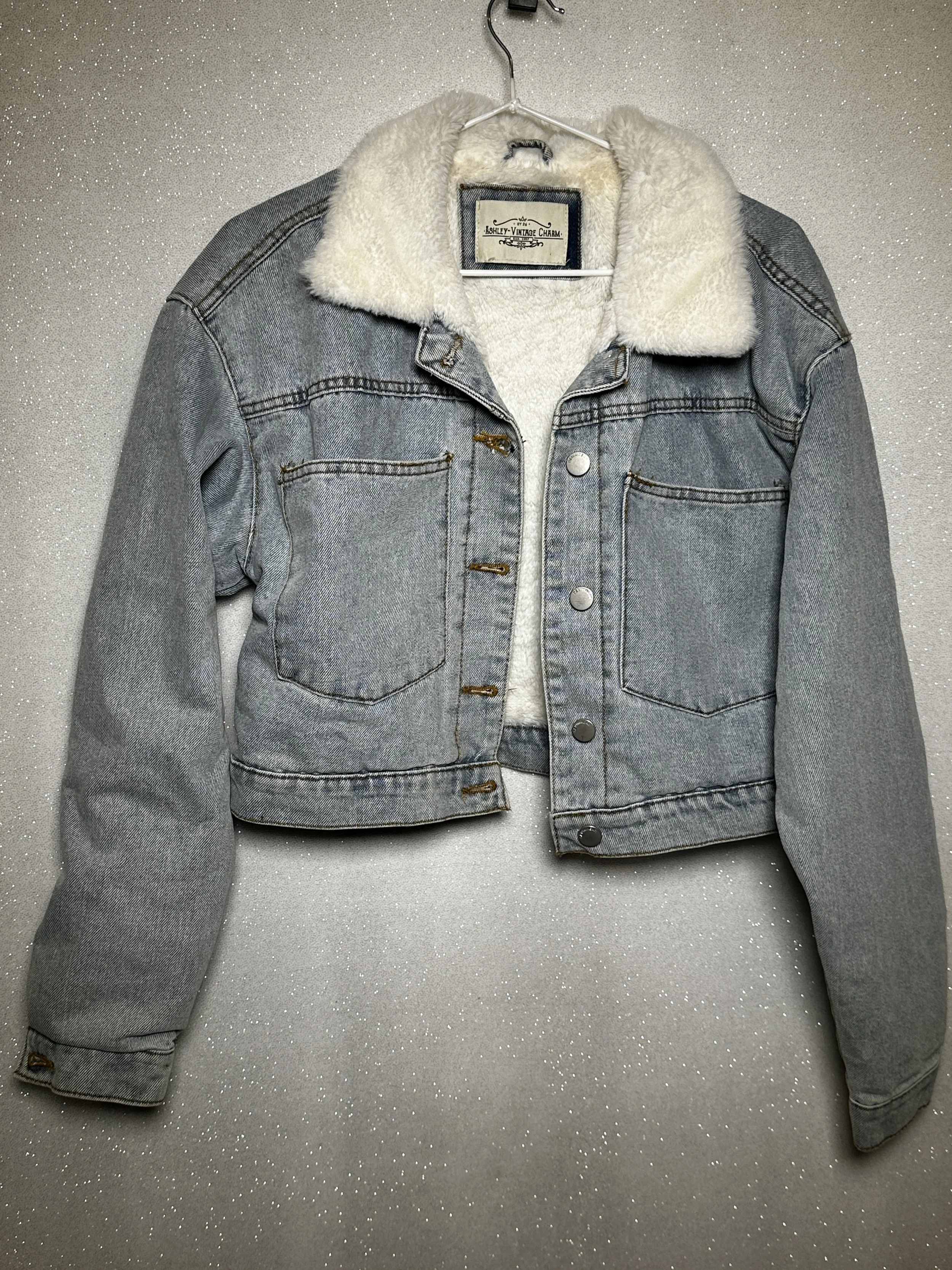 Grey denim jacket with a cream faux shearling collar hanging on a metal hanger.