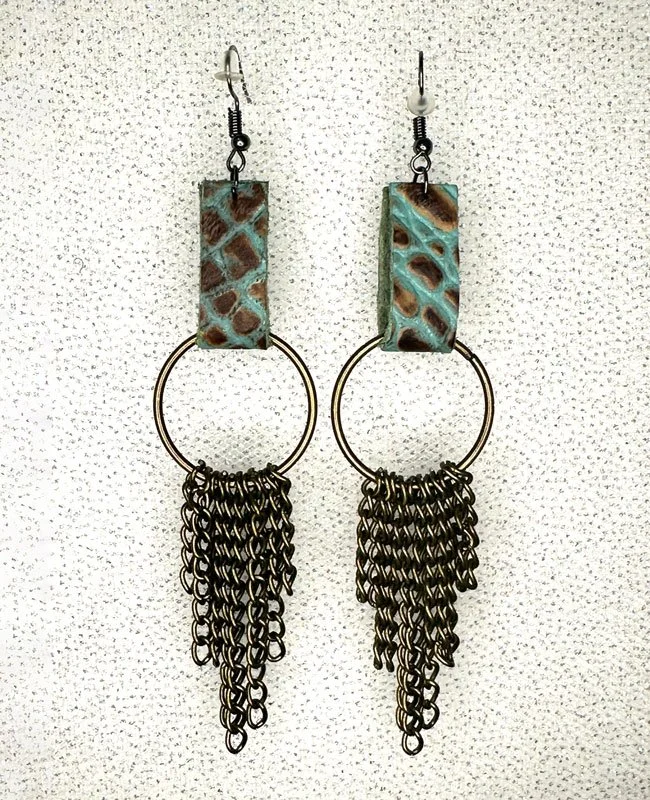 Pair of earrings with rectangular turquoise-colored stones, circular metal rings, and cascading black chains, displayed on a textured light background.