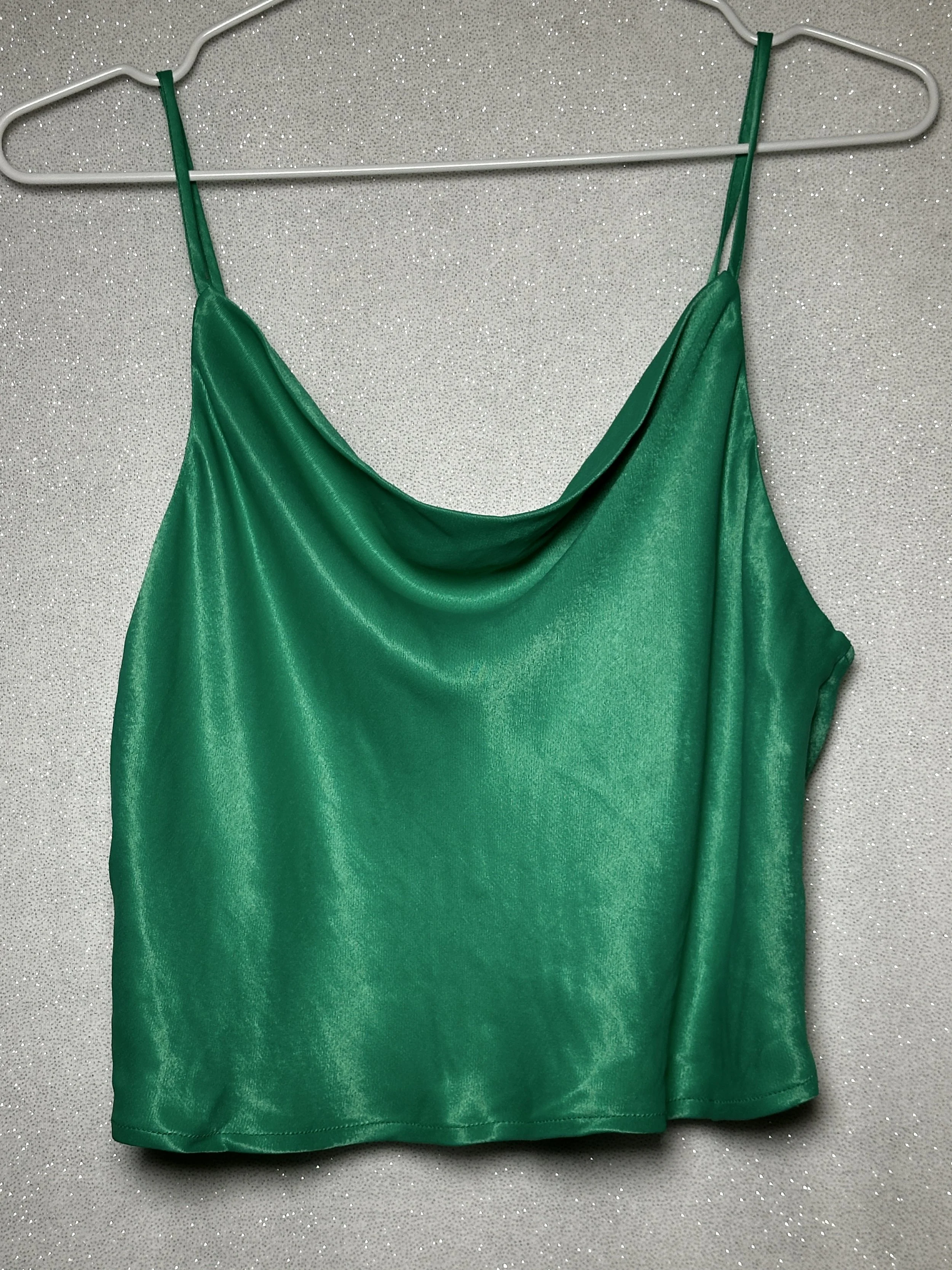 Green satin sleeveless top hanging on a hanger against a sparkly silver background.