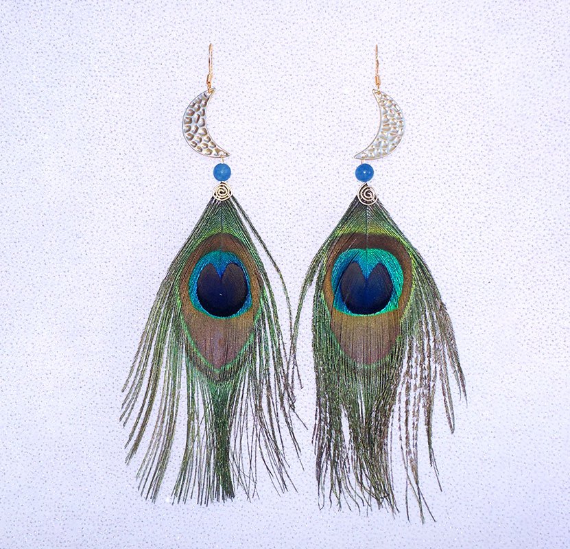 A pair of earrings shaped like peacock feathers hanging from crescent moon-shaped hooks, with blue beads and intricate wire coiling at the top.