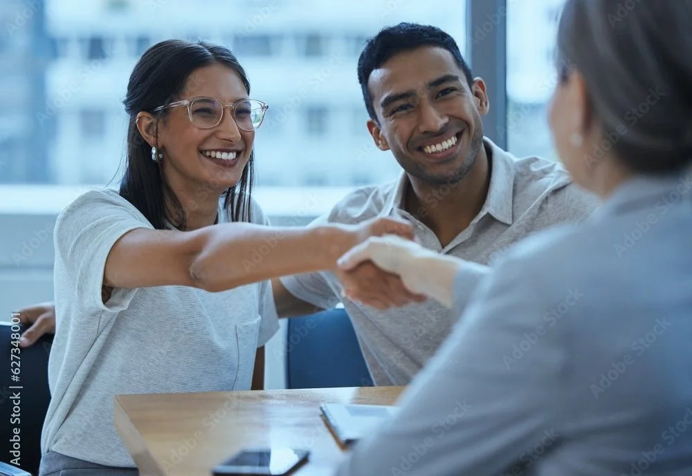 A woman and man smiling and shaking hands with an interviewee in a professional setting.