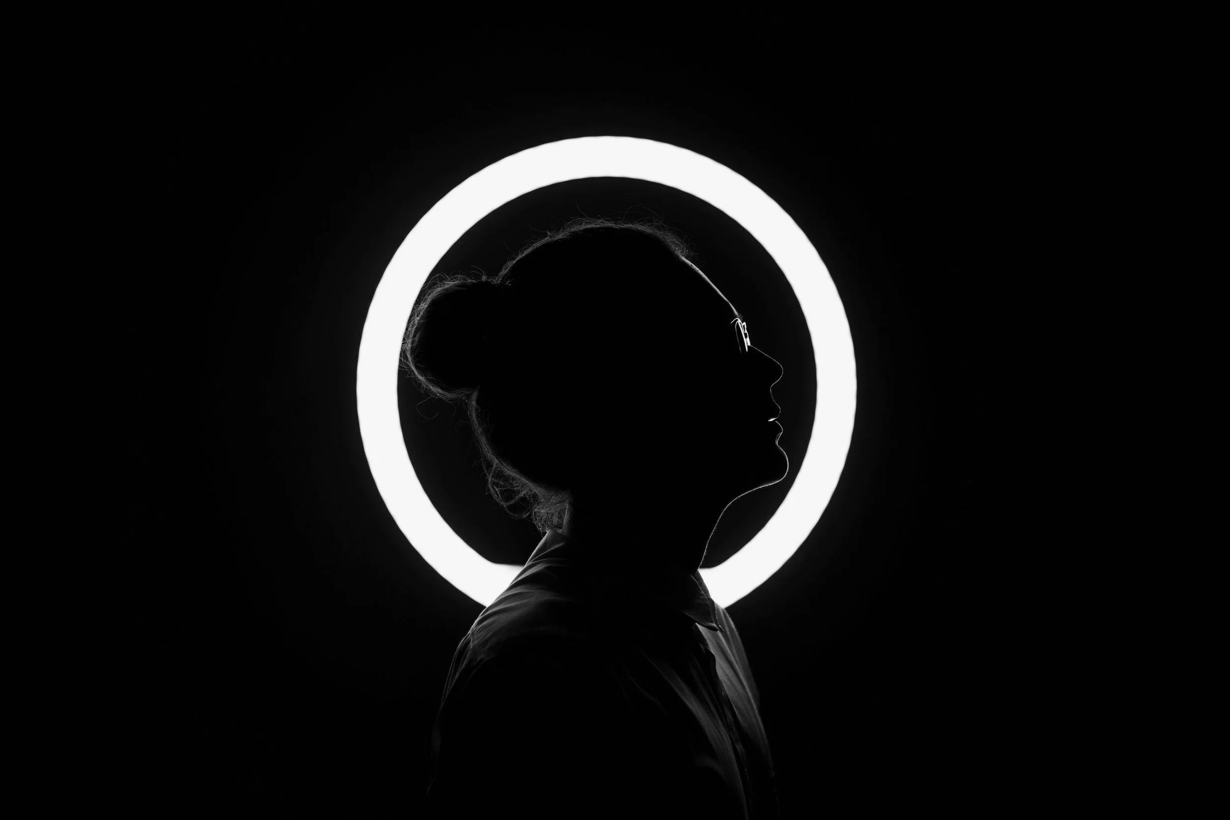 Silhouette of a woman with glasses in profile against a dark background with a circular neon light behind her.
