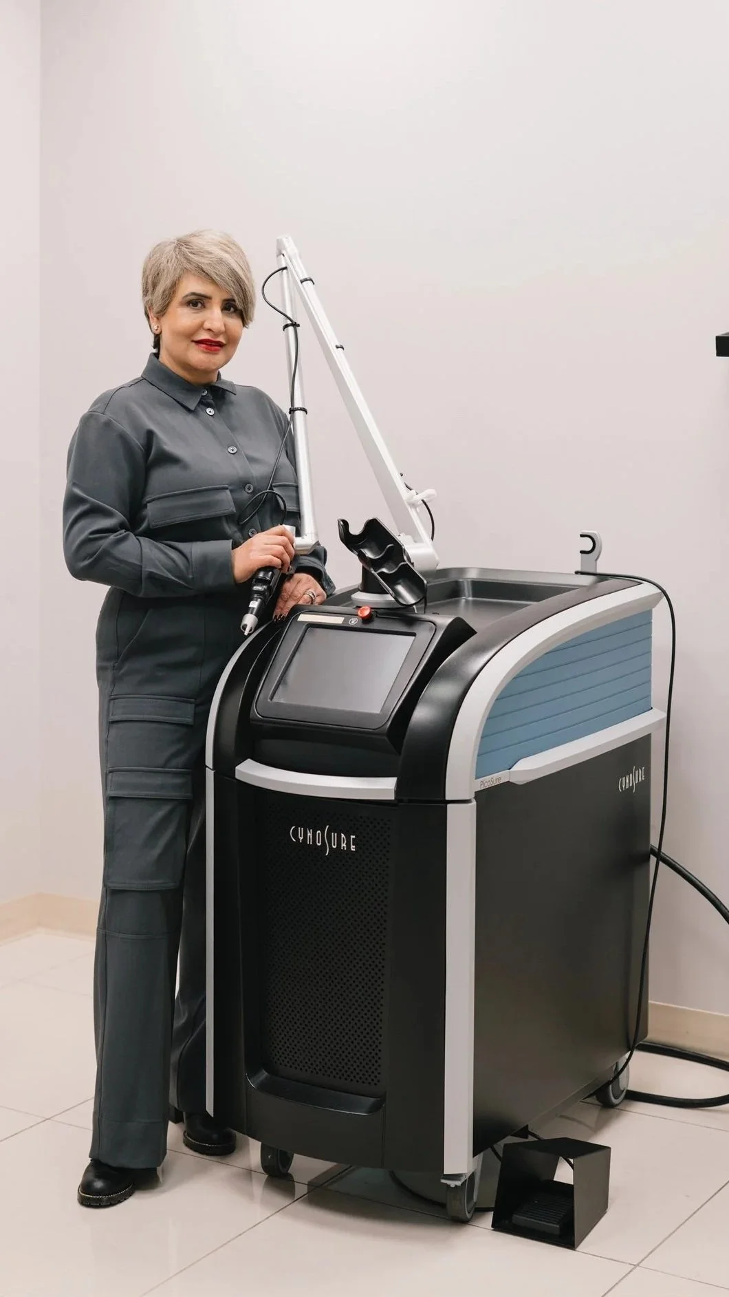 A woman in gray uniform standing next to a medical laser machine in a clinical setting.