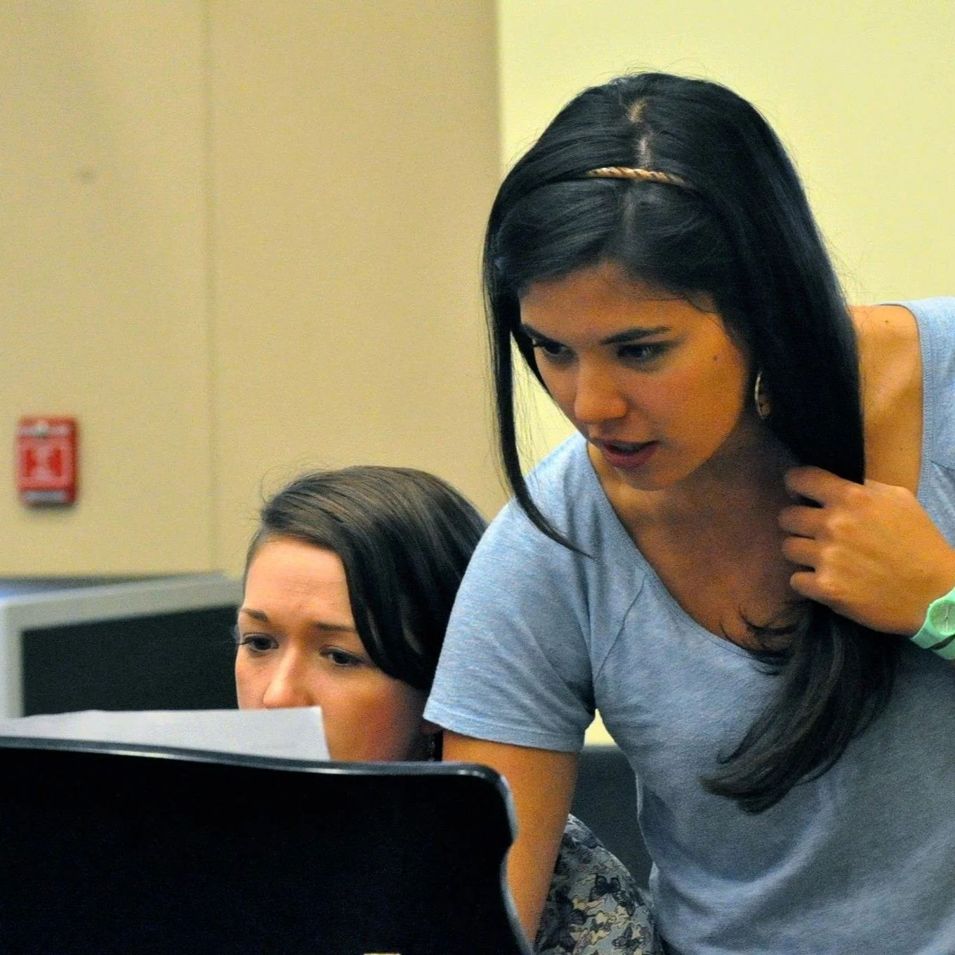 Two women working together at a computer in an office setting.