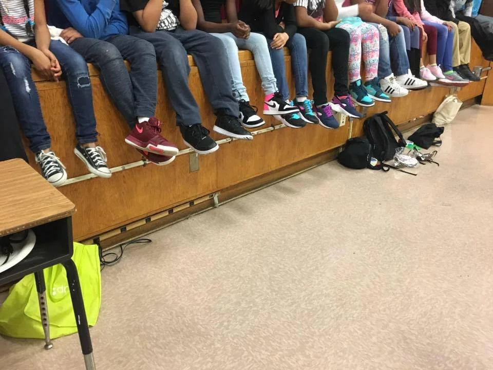 Students sitting on a bench, with their legs hanging over the edge, wearing various sneakers and jeans.