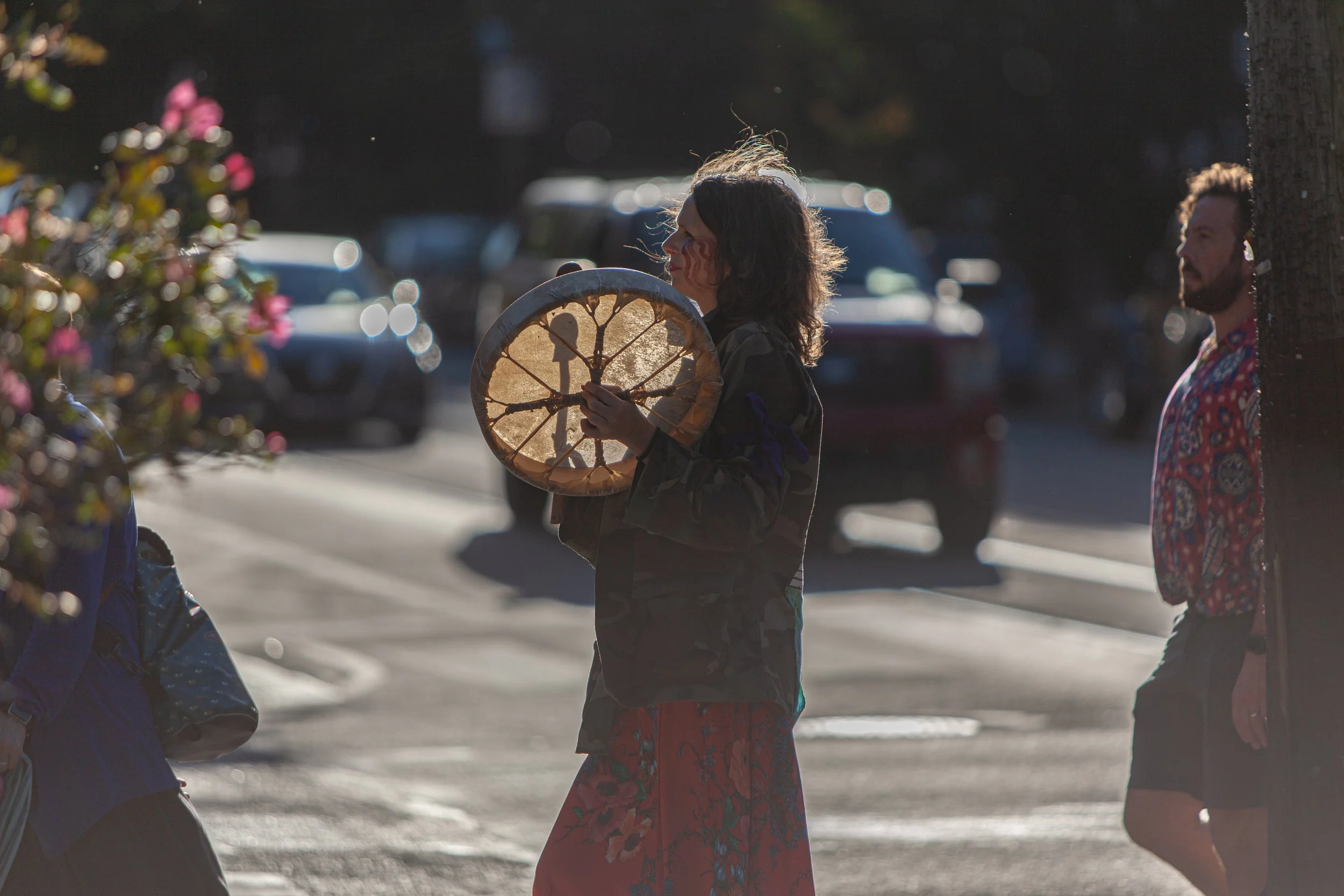Person holding a hand drum walking on a city street with blurred cars in the background.