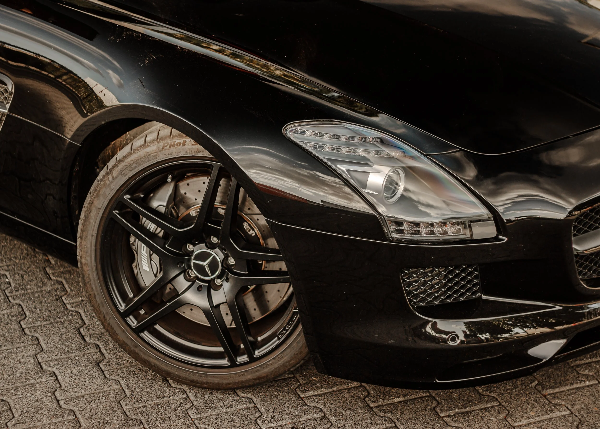 Schwarzer Mercedes-Benz Sportwagen mit schwarzer Felge und Bremsscheibe auf gepflasterter Straße.