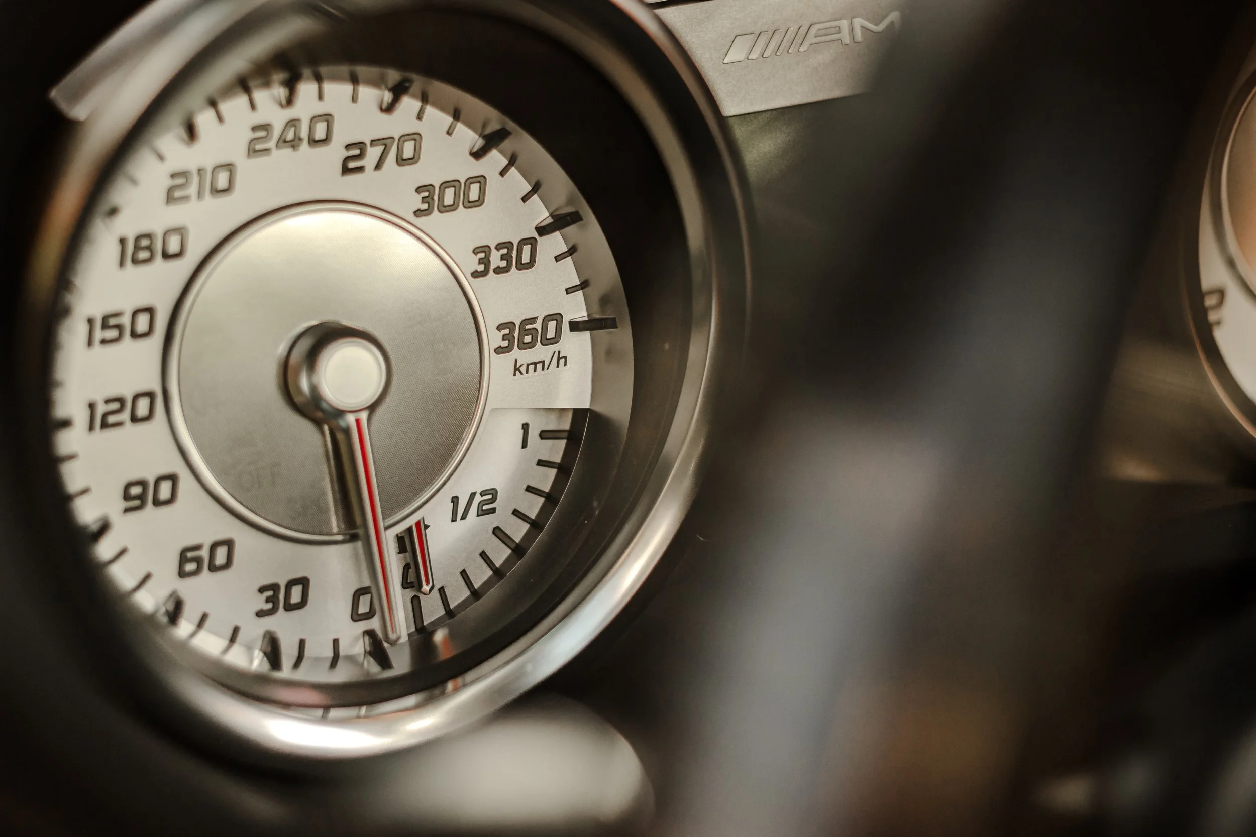 Automobil-Tachometer mit Geschwindigkeitsmesser, Anzeige im Bereich von 0 bis 360 km/h, Nadel zeigt etwa 0 km/h, teilweise sichtbare Marken und Zeiger. Das Dashboard trägt ein AMG-Logo.